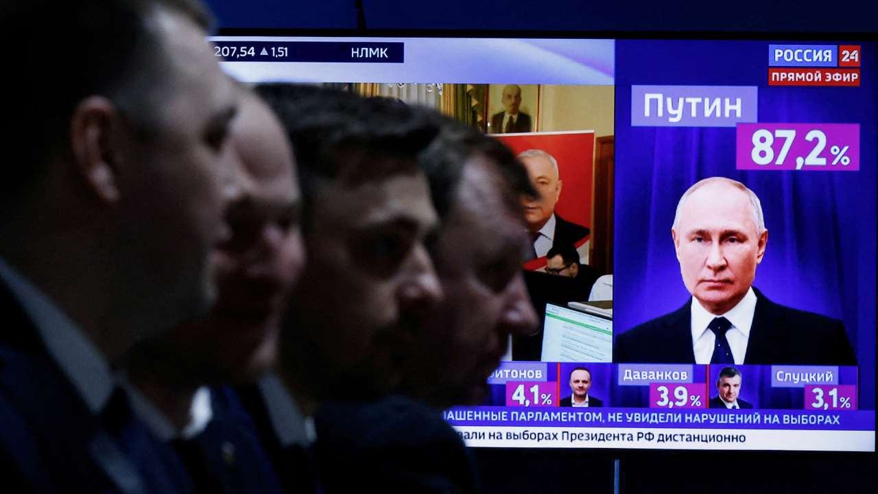 Men sit near a TV broadcasting news on the results of Russian incumbent President Putin, in Moscow