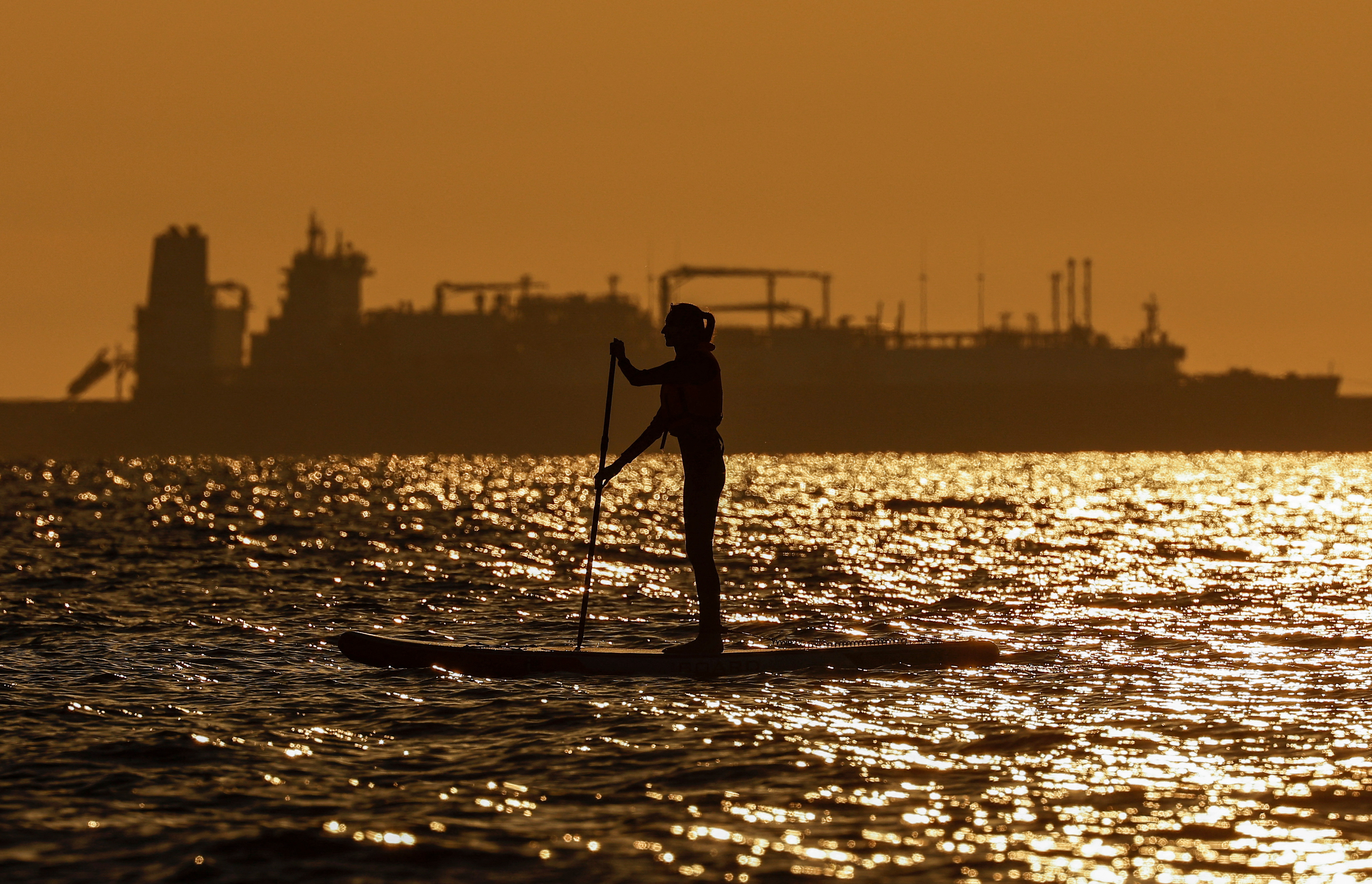 A paddleboarder rows in front of an LNG carrier in Zelenogradsk