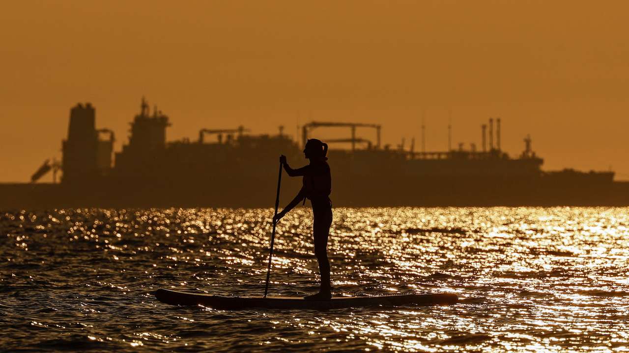 A paddleboarder rows in front of an LNG carrier in Zelenogradsk