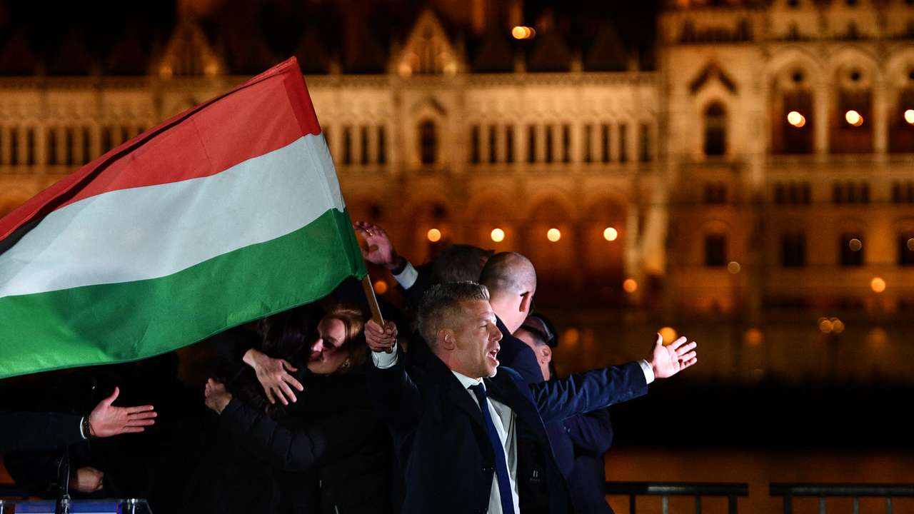 Peter Magyar, leader of the pro-European conservative TISZA party, waves the national flag on the banks on the river Danube with the Parliament building in the background, during their election night party in Budapest during the general election in Hungary, on April 12, 2026. Polls closed in Hungary's parliamentary election, with turnout reaching a record high in the crunch vote that sees nationalist Prime Minister Viktor Orban's 16-year stint in power face an unprecedented challenge from conservative political newcomer Peter Magyar. (Photo by Ferenc ISZA / AFP)