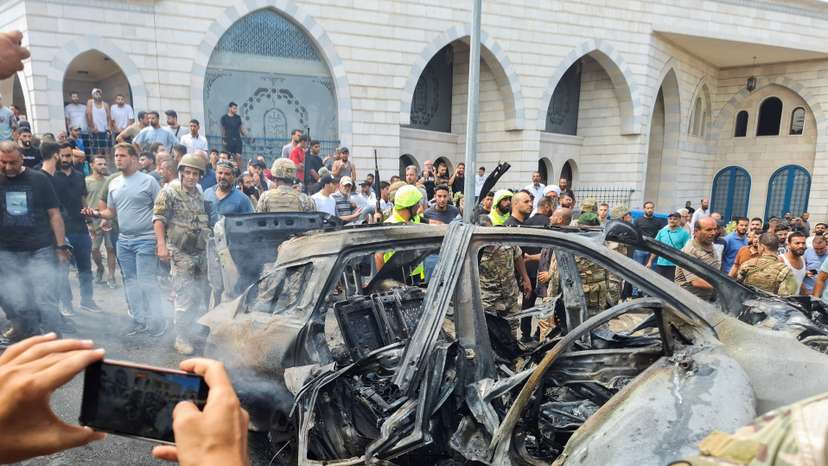 A man uses his phone as he stands near a burnt car after an Israeli strike on the outskirts of the southern port city of Sidon, according to two Palestinian sources