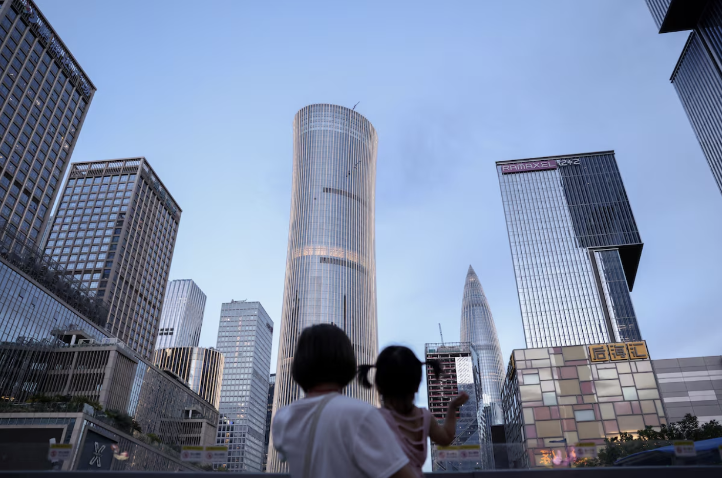 A woman holds a child near office buildings in Shenzhen, Guangdong province, China September 15, 2025. REUTERS/Tingshu Wang/File Pho
