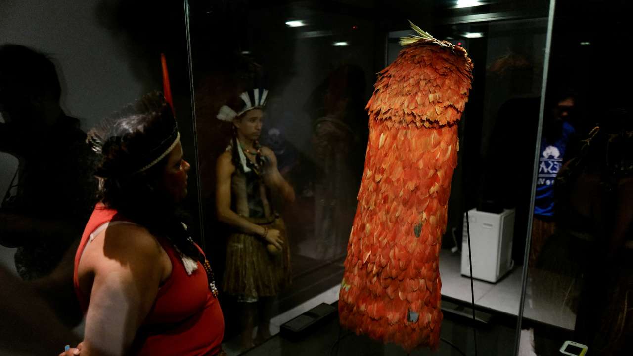Indigenous people stand next to the Tupinamba cloak, a feathered ceremonial cape used in religious rituals, at the Brazil's National Museum in Rio de Janeiro