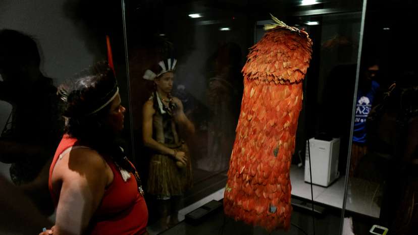 Indigenous people stand next to the Tupinamba cloak, a feathered ceremonial cape used in religious rituals, at the Brazil's National Museum in Rio de Janeiro