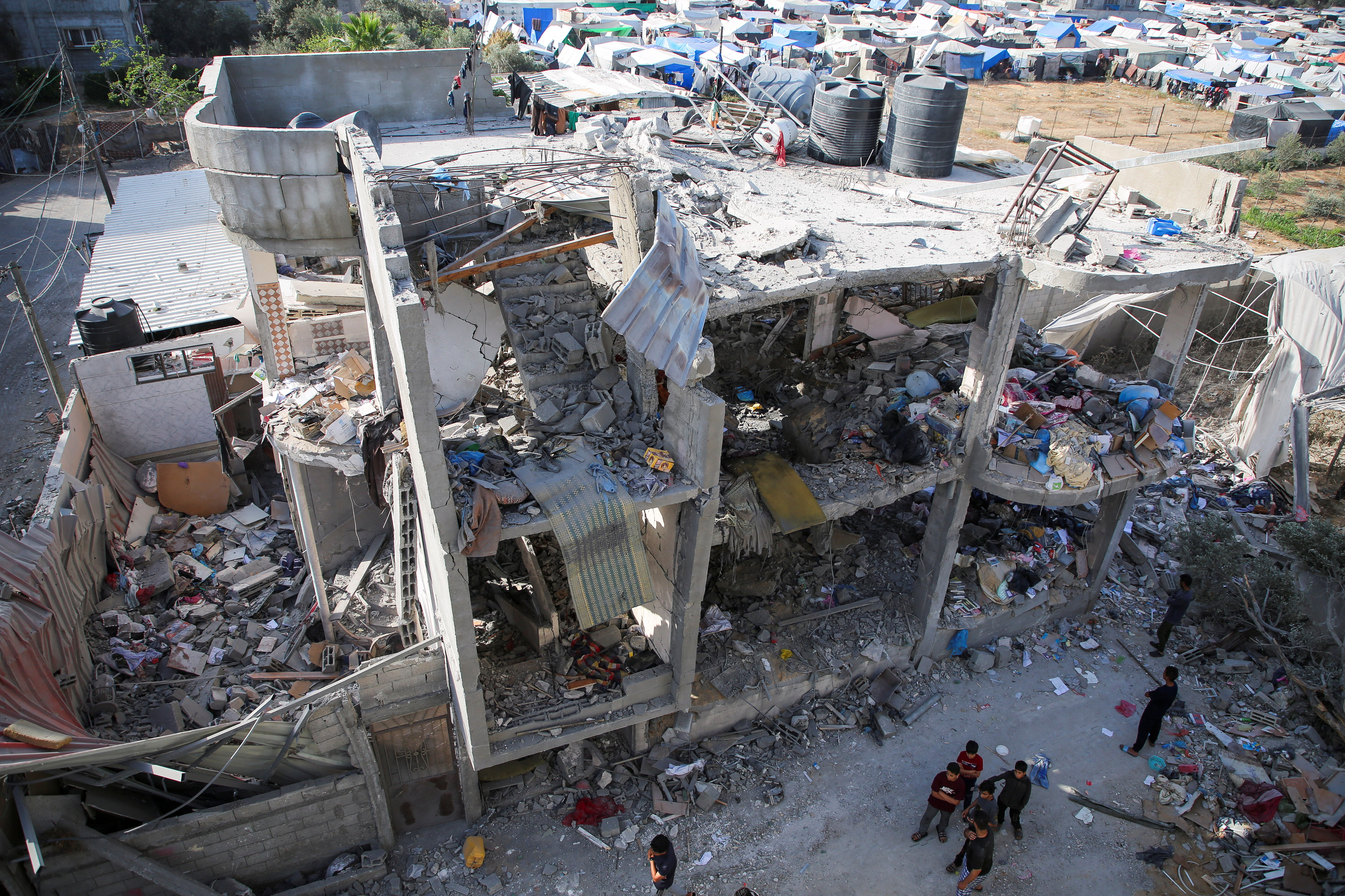 People stand next to a house damaged in an Israeli strike, amid the ongoing conflict between Israel and the Palestinian Islamist group Hamas, in Rafah