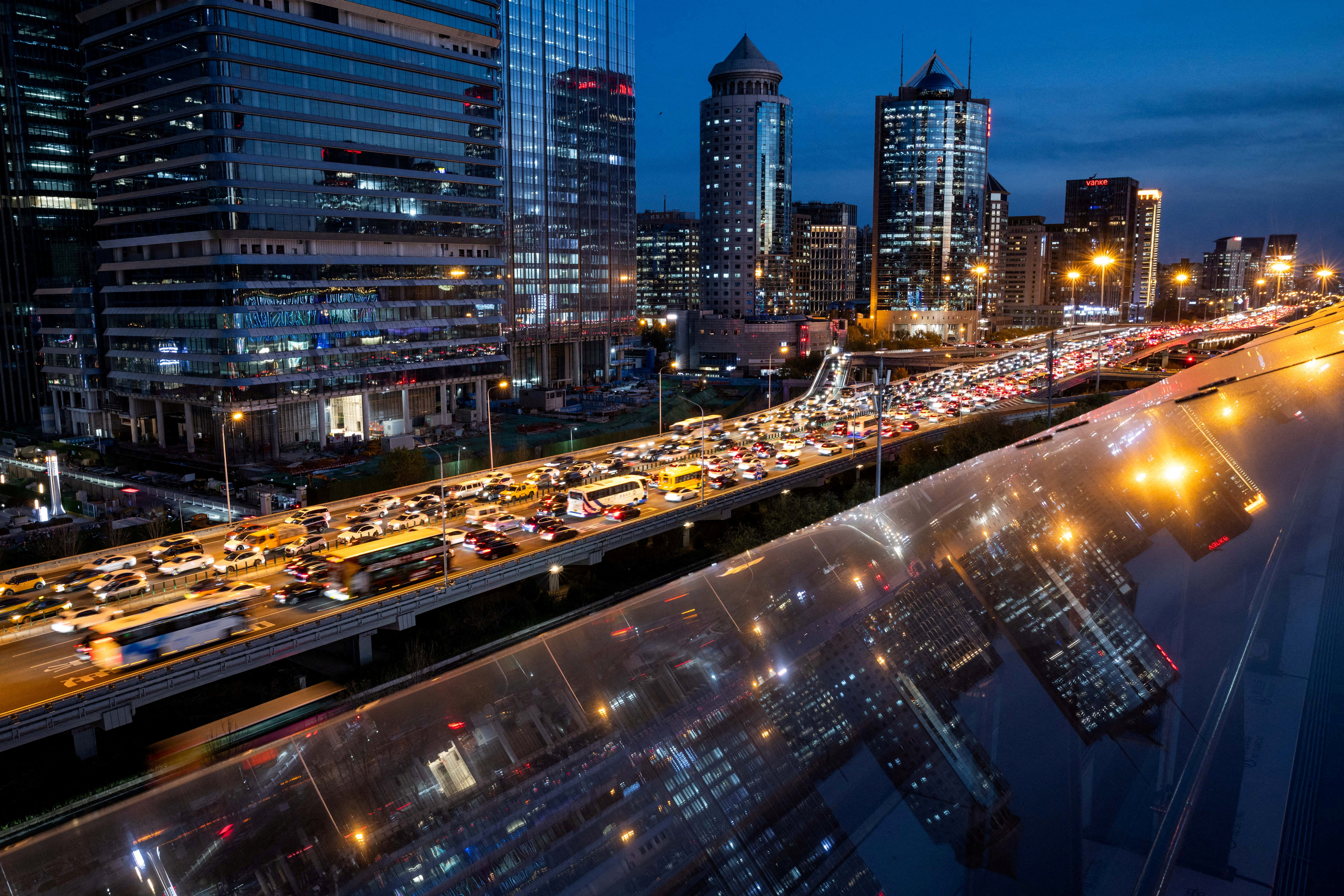 Cars are stuck in traffic on an elevated highway as buildings are reflected on a glass surface in Beijing's central business district