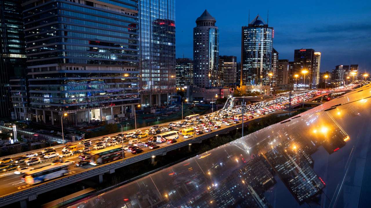 Cars are stuck in traffic on an elevated highway as buildings are reflected on a glass surface in Beijing's central business district
