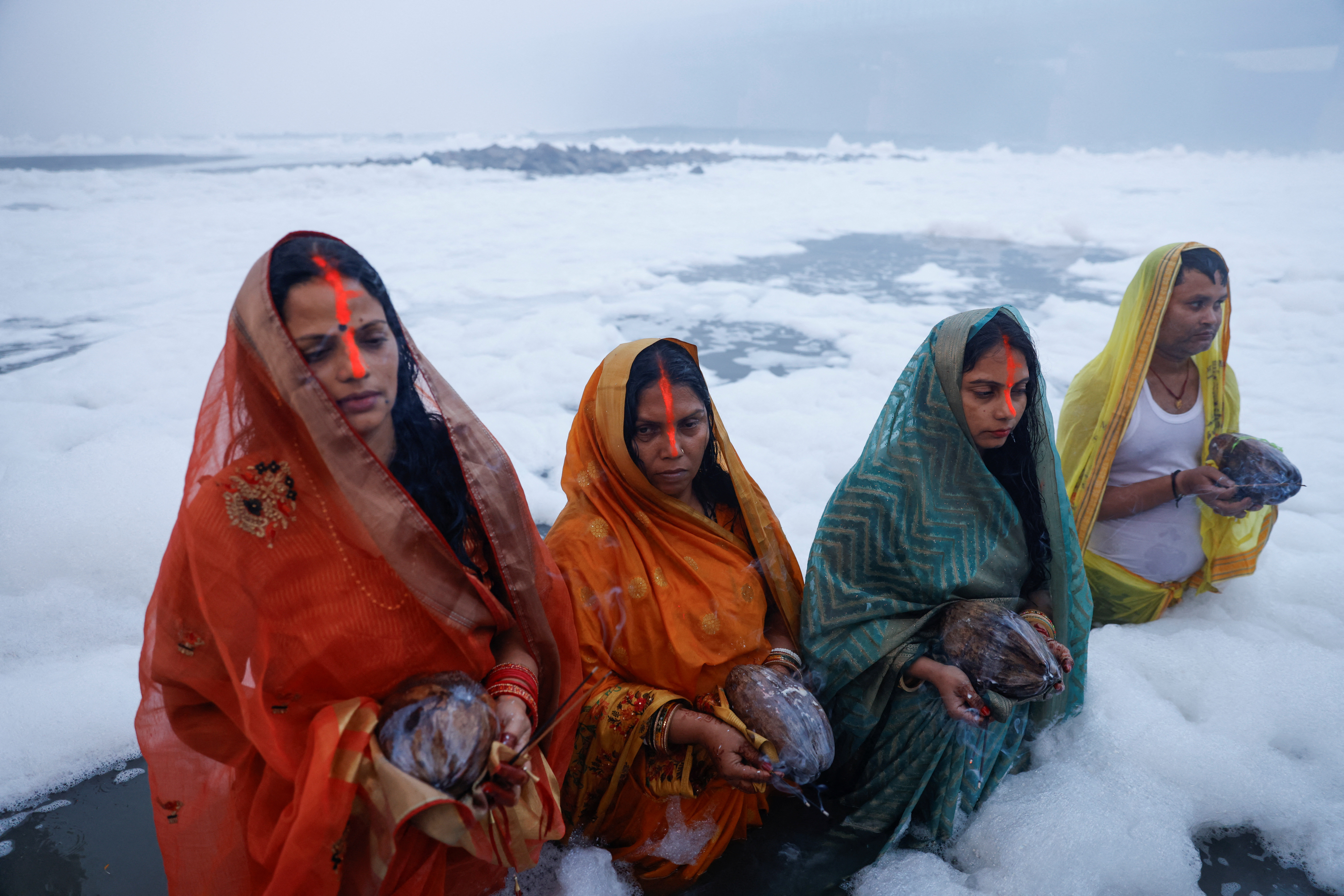 Hindu devotees worship the Sun god as they stand amidst the foam covering the polluted Yamuna river during the Hindu religious festival of Chhath Puja on a smoggy morning in New Delhi