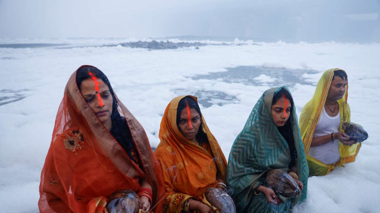 Hindu devotees worship the Sun god as they stand amidst the foam covering the polluted Yamuna river during the Hindu religious festival of Chhath Puja on a smoggy morning in New Delhi
