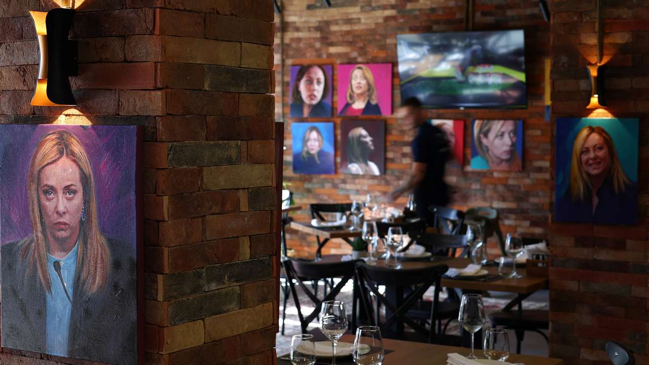 A waiter stands as portrait paintings by artist Helidon Haliti of Italy's Prime Minister Giorgia Meloni are seen on the walls of "Trattoria Meloni" just outside a migrant processing camp set up by the Italian government, in Shengjin