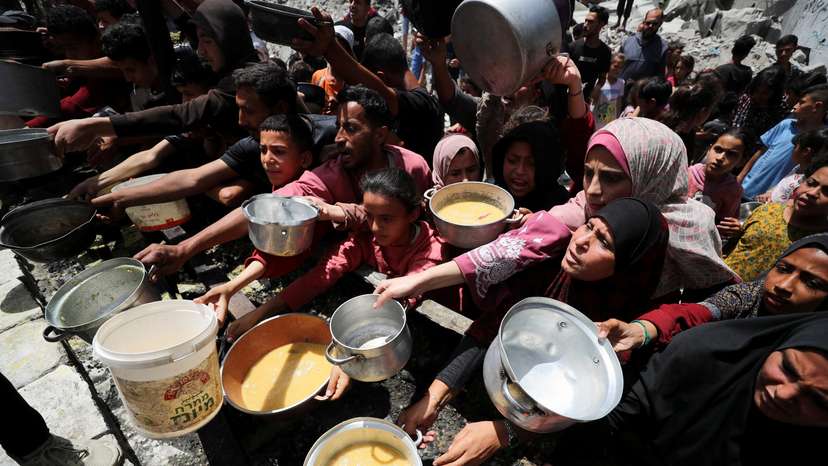 Palestinians wait to receive food cooked by a charity kitchen, in Jabalia, in the northern Gaza Strip