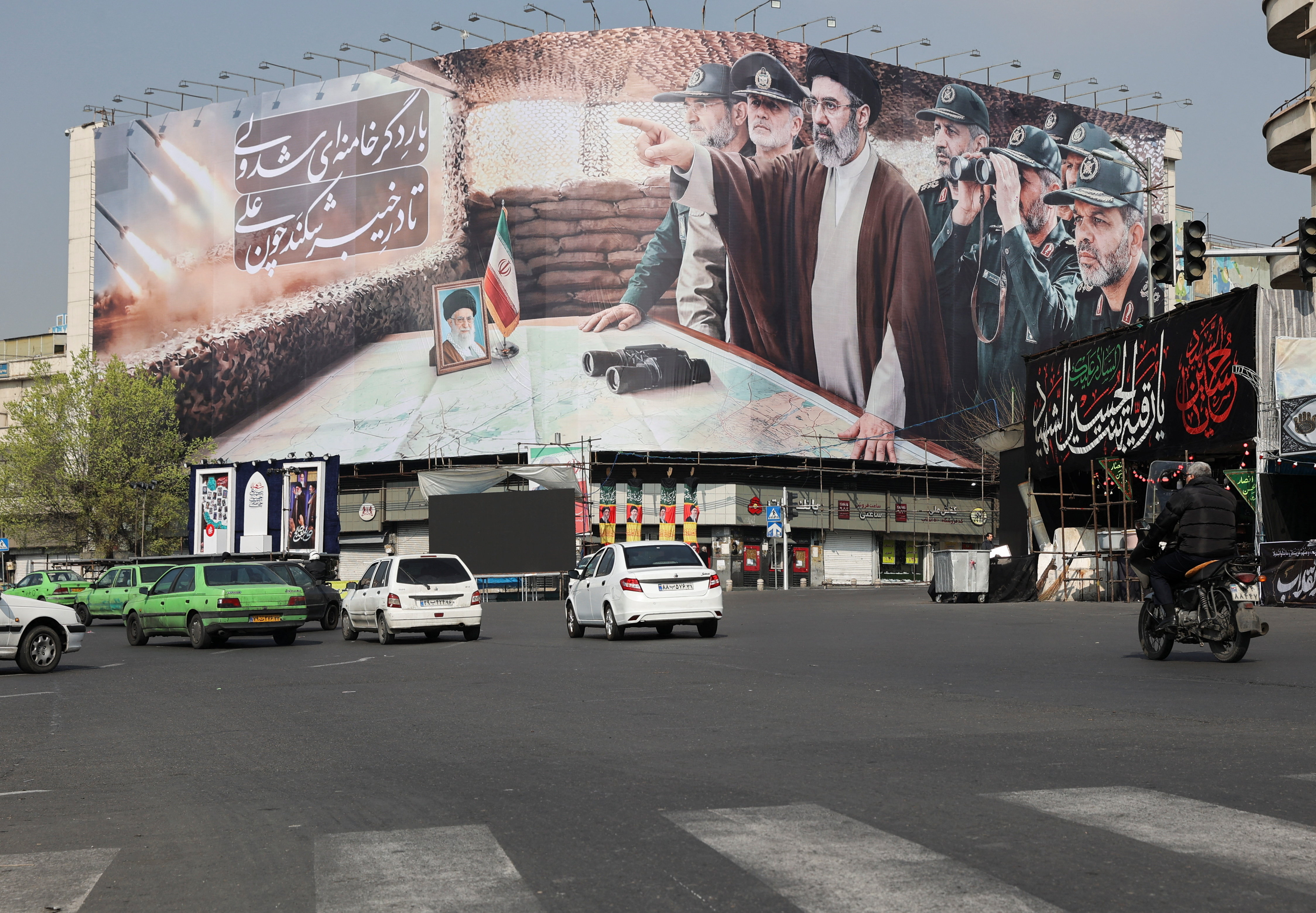 Cars pass a banner featuring Iran's new Supreme Leader Mojtaba Khamenei, in Tehran