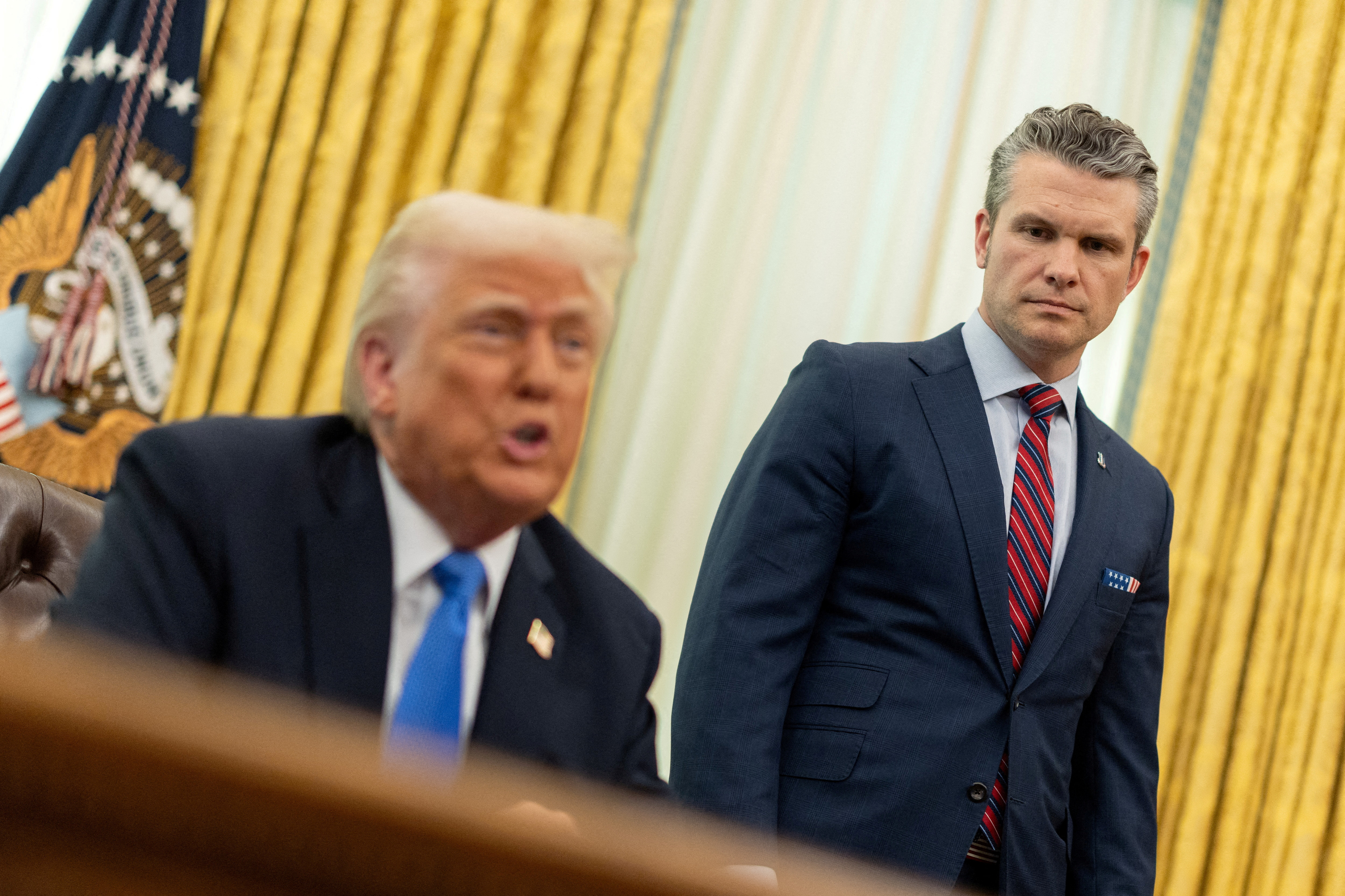 FILE PHOTO: U.S. Defense Secretary Pete Hegseth speaks next to President Donald Trump, in the Oval Office at the White House, in Washington, D.C.
