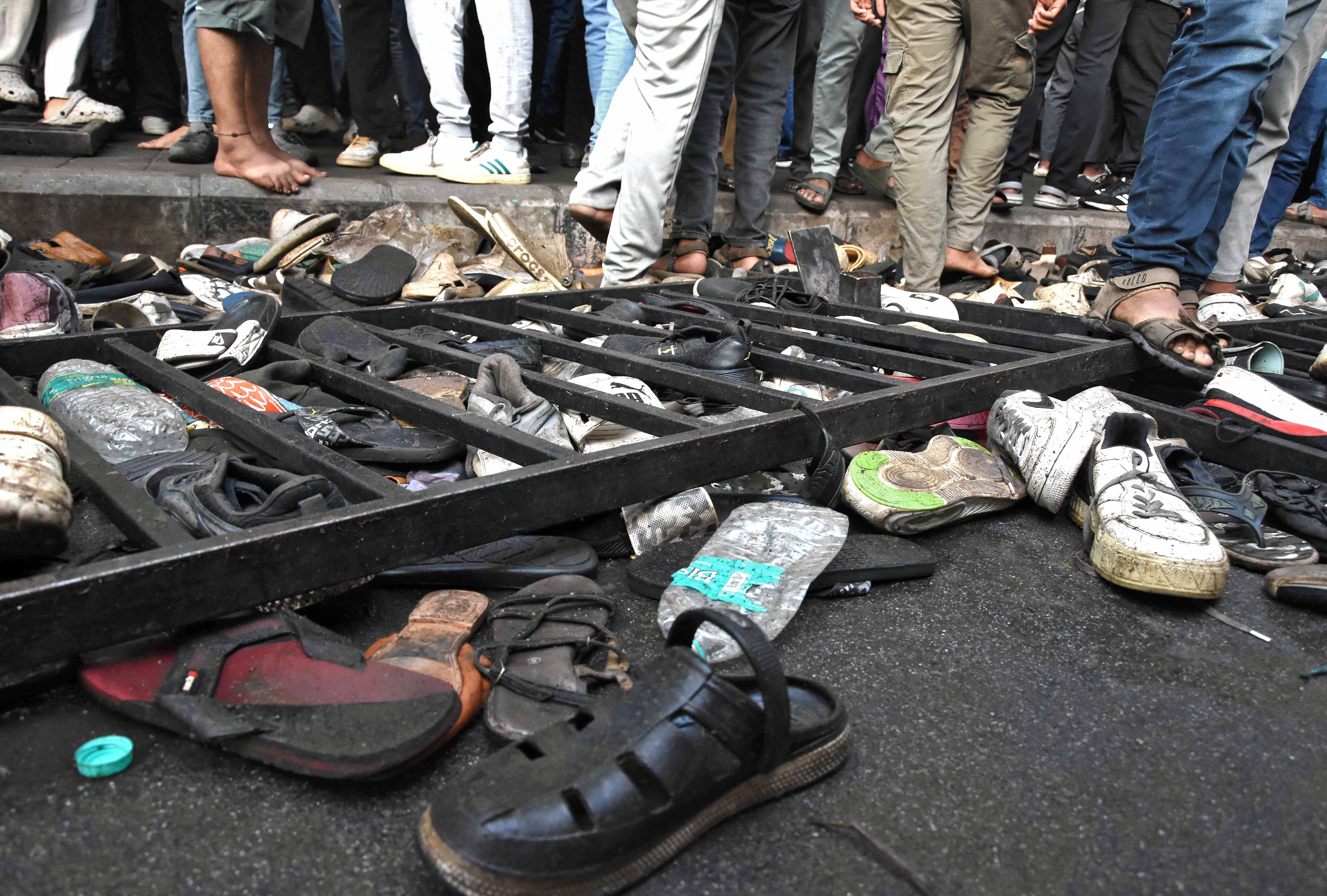 People walk past shoes left behind following a stampede outside a cricket stadium in Bengaluru