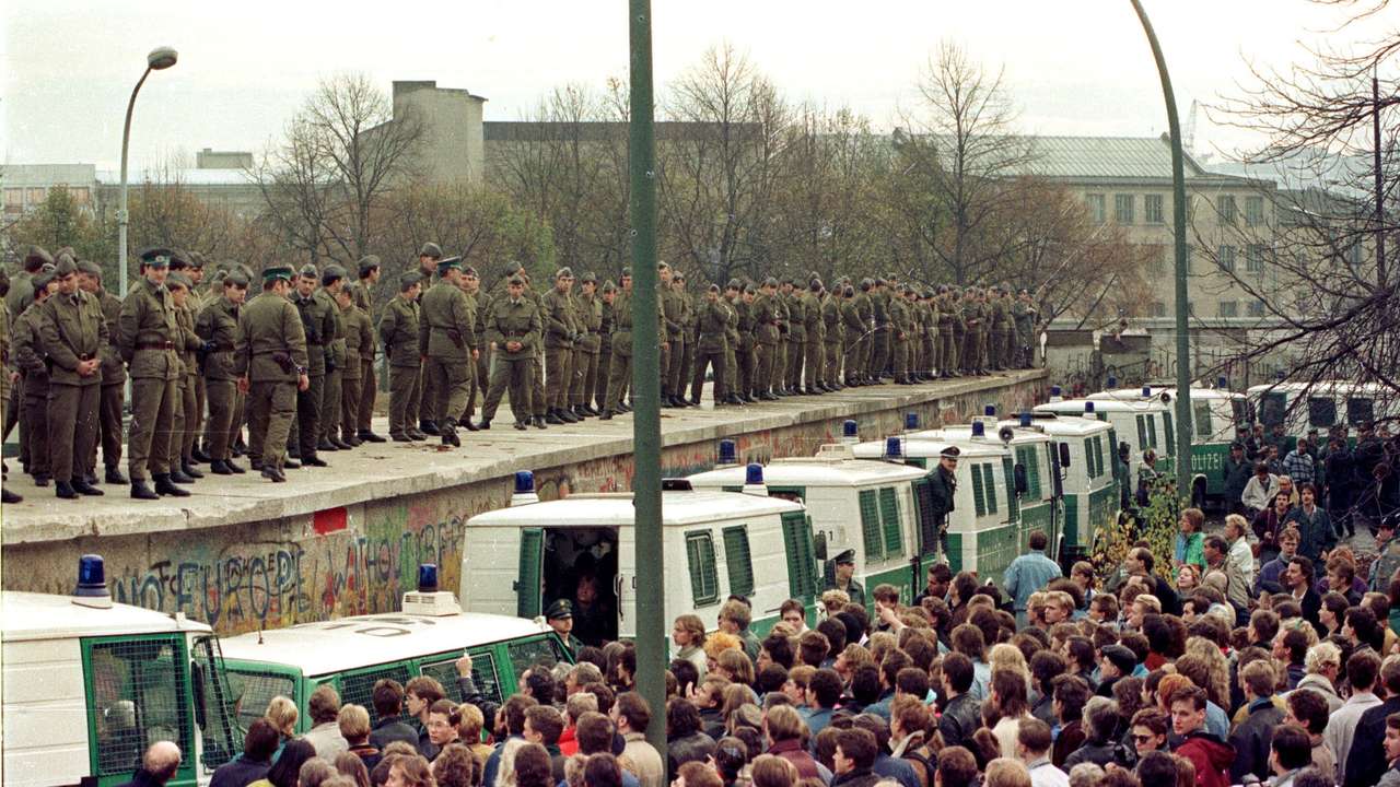 FILE PHOTO: East Berlin border guards stand atop the Berlin Wall at the Brandeburg Gate faced by thousands of West Berliners on November 11, 1989.
