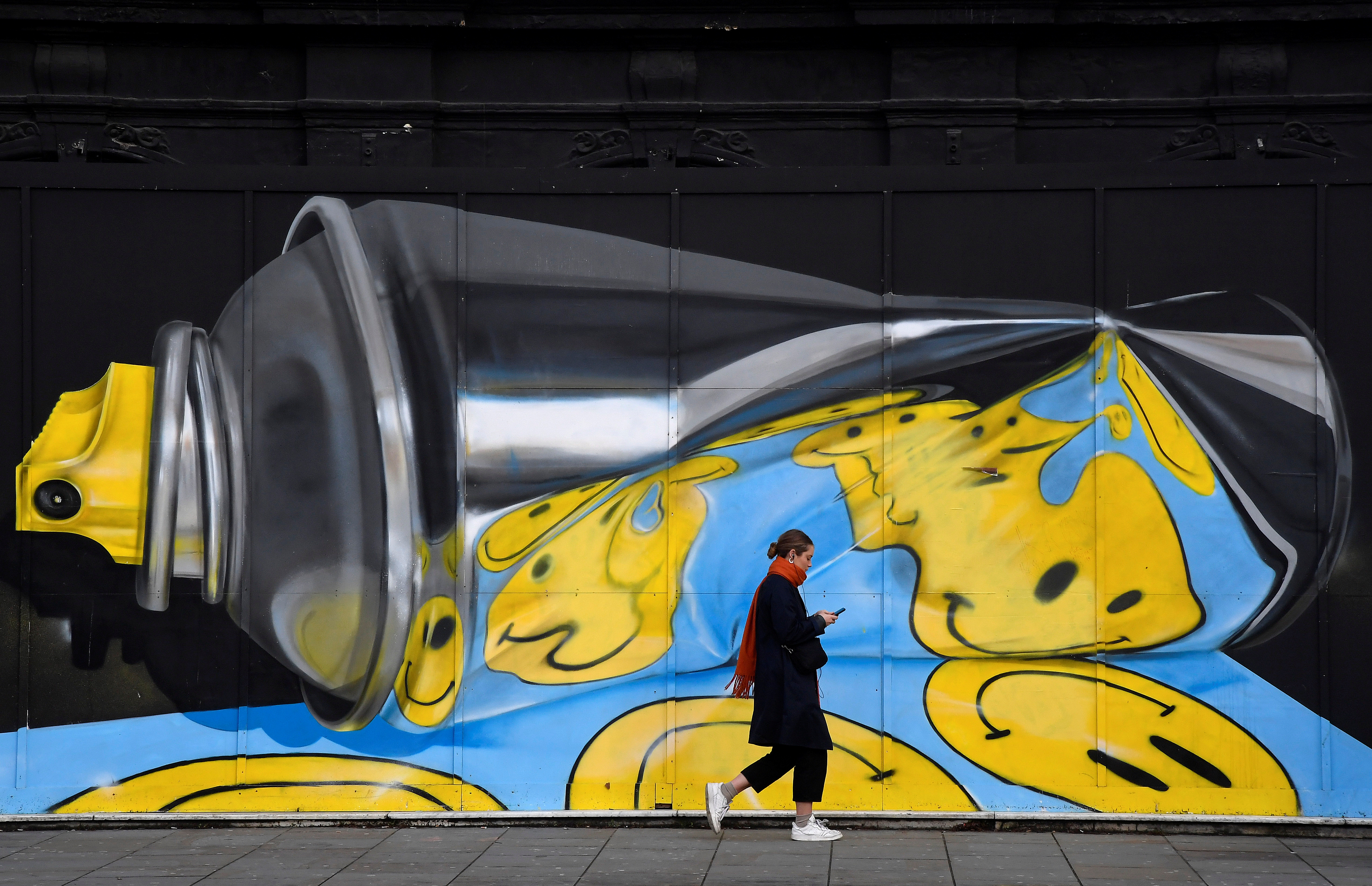 A woman views her phone as she walks past street art on a wall in London, Britain