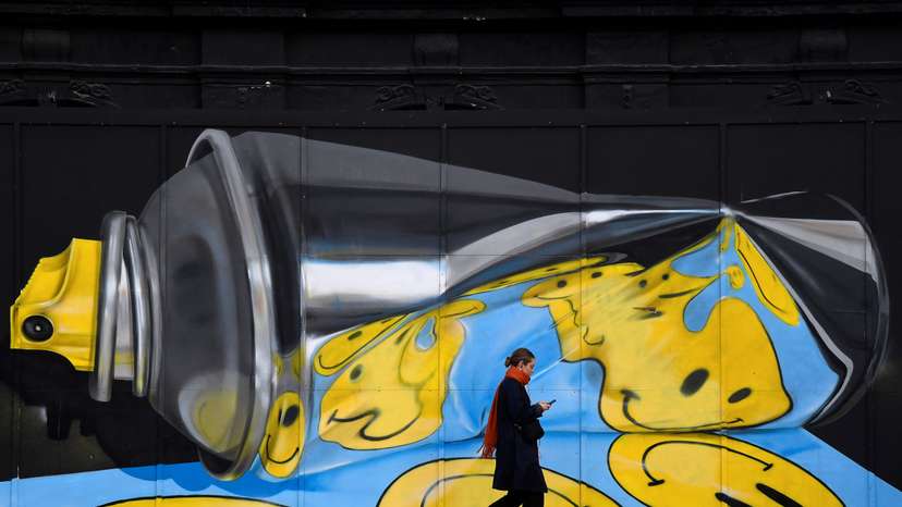 A woman views her phone as she walks past street art on a wall in London, Britain