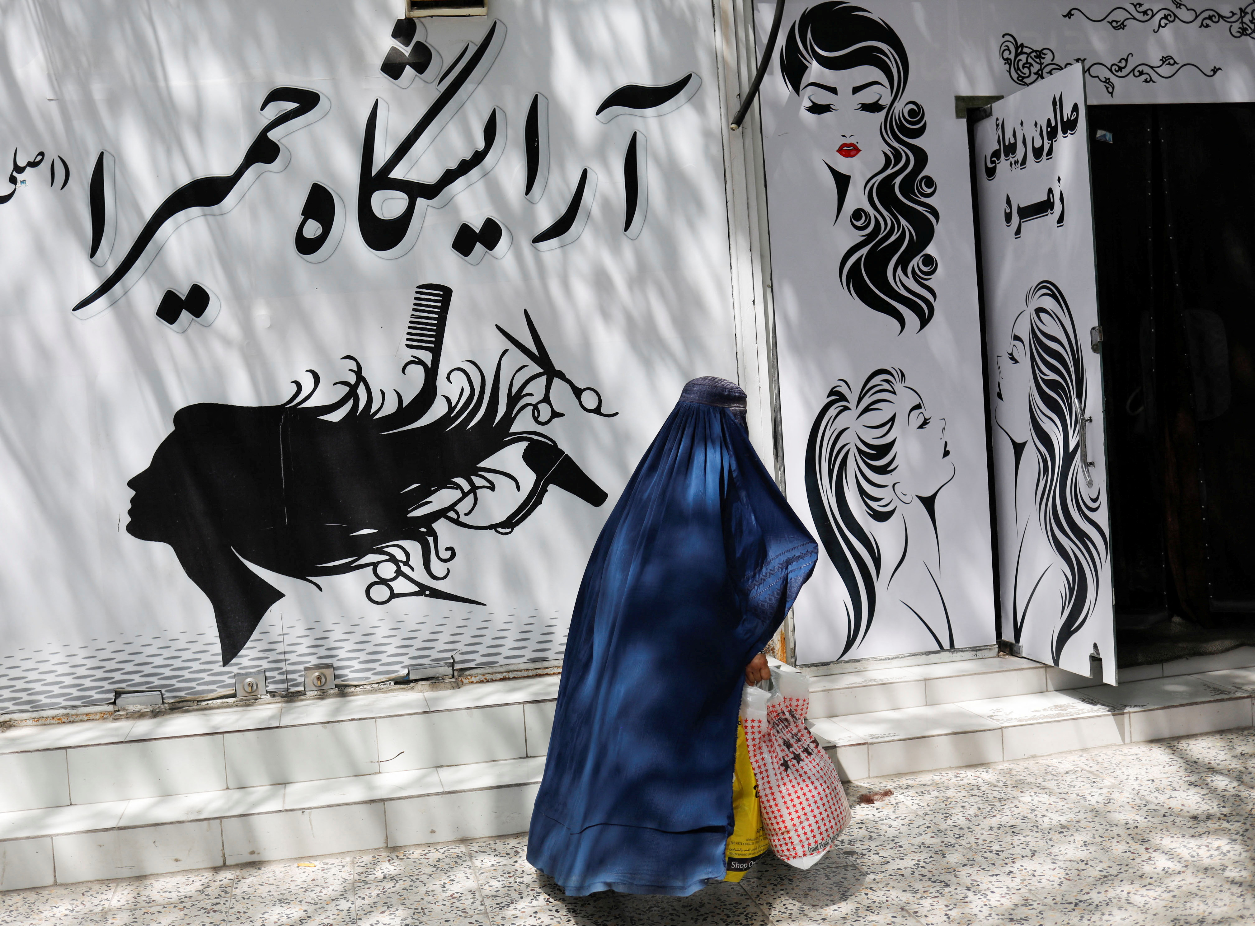 An Afghan woman walks past a beauty salon in Kabul