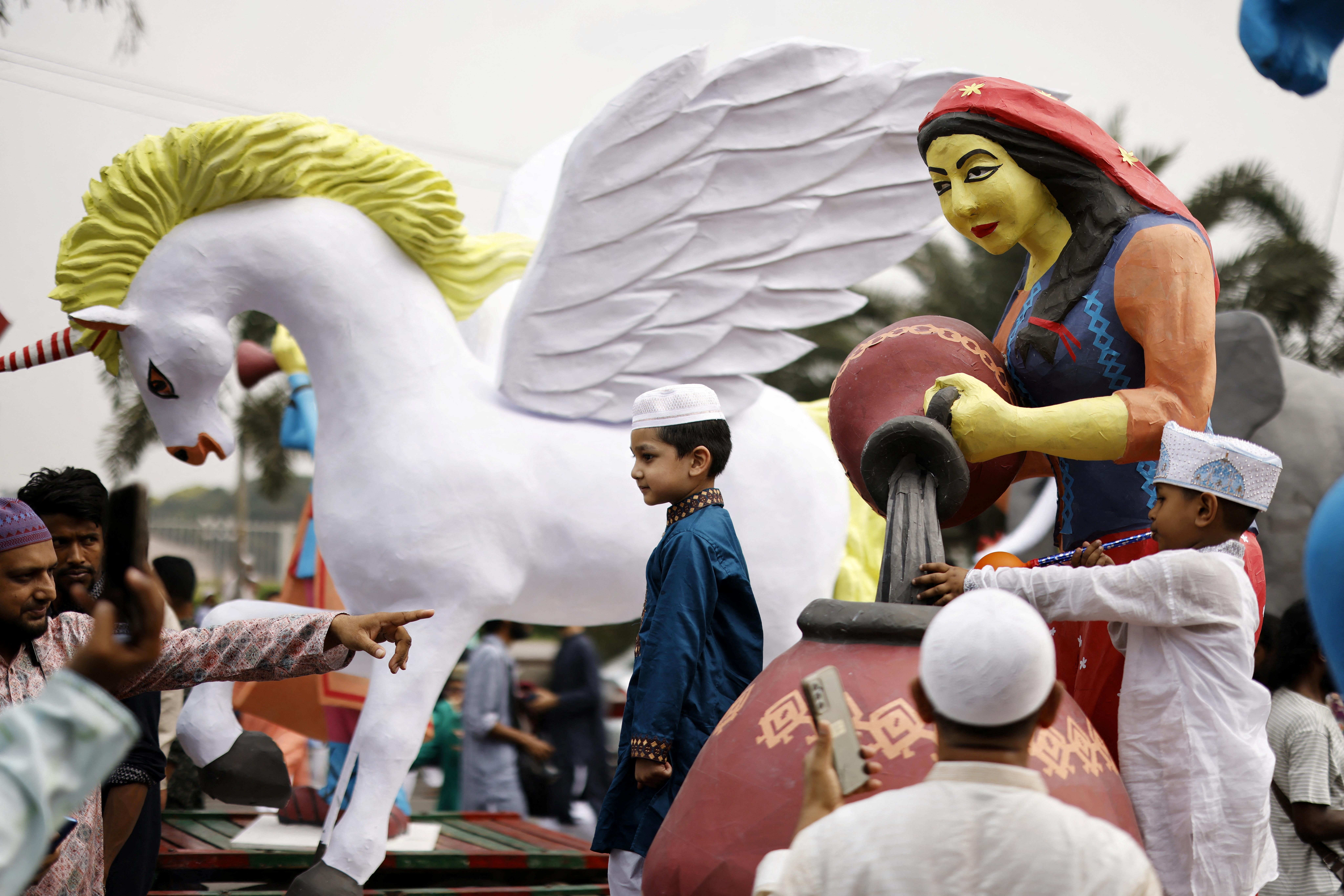Children take pictures with makeshift sculptures brought to an Eid al-Fitr rally to mark the end of the holy month of Ramadan, in Dhaka
