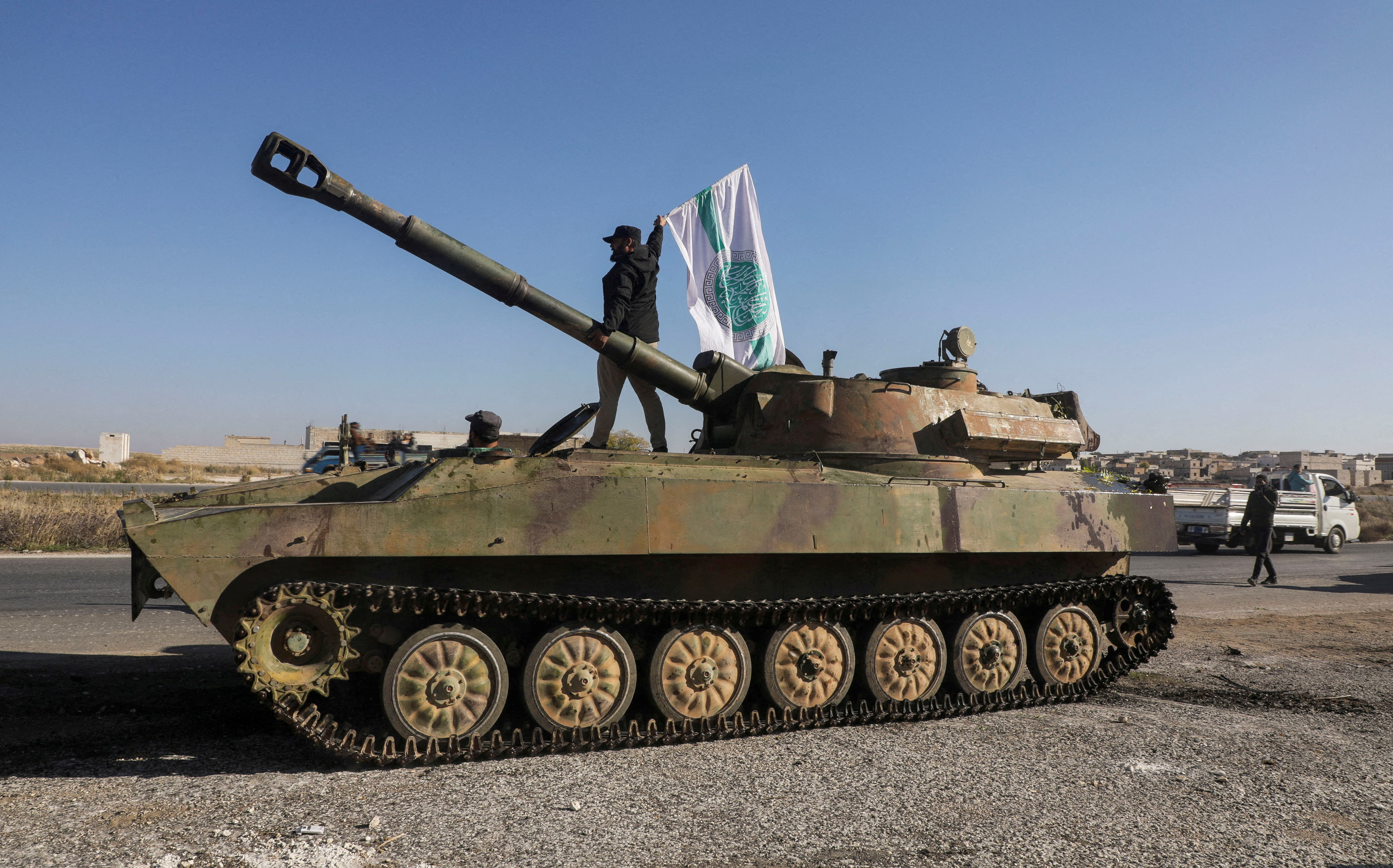 A rebel fighter stands atop a military vehicle as he carries a Hayat Tahrir al-Sham flag in Saraqeb