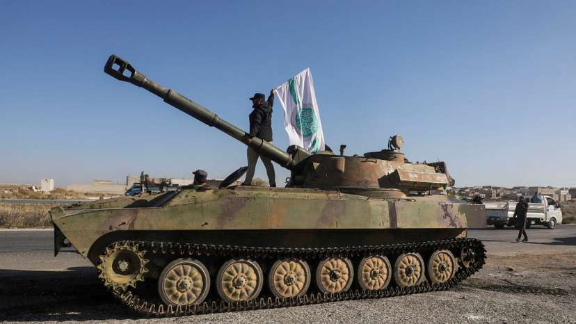 A rebel fighter stands atop a military vehicle as he carries a Hayat Tahrir al-Sham flag in Saraqeb