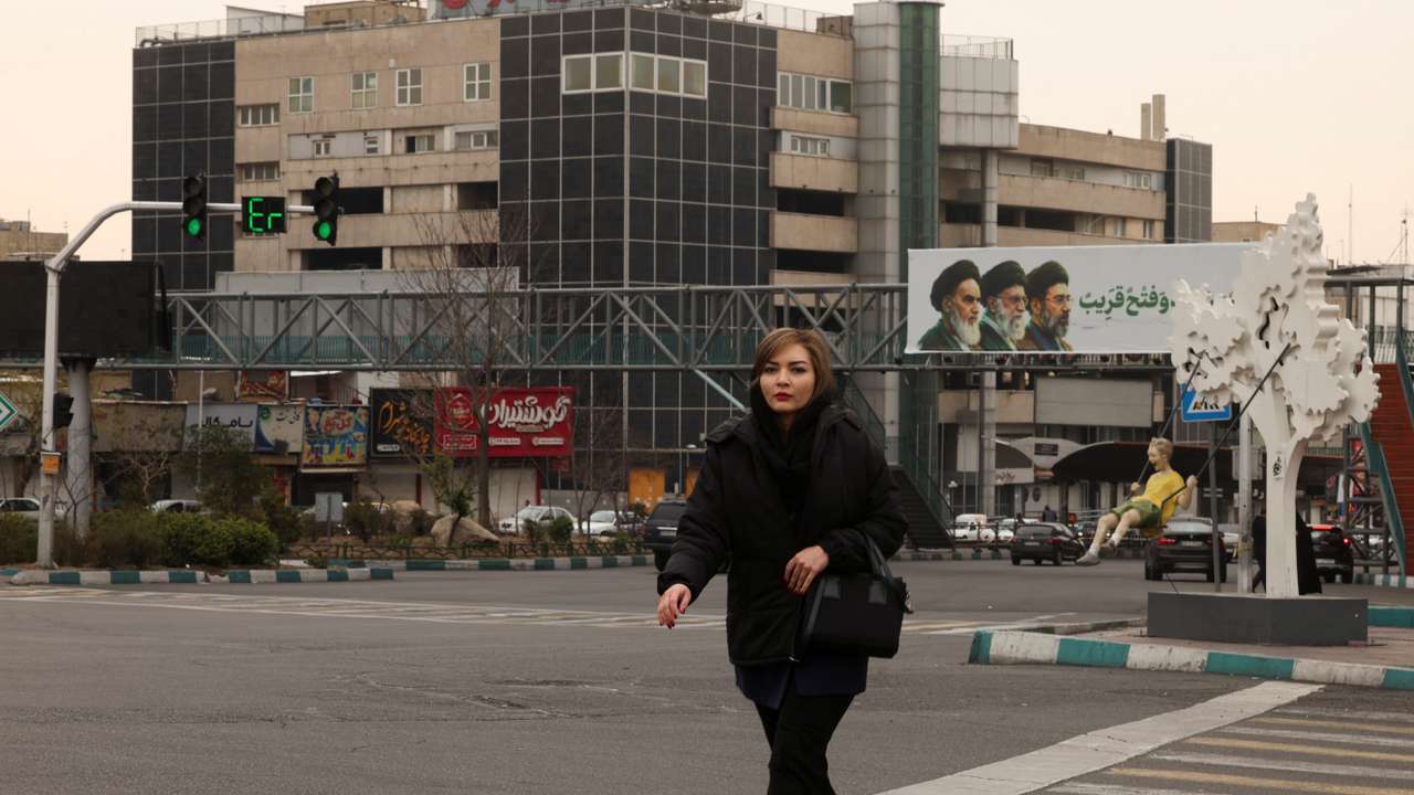 A woman walks across the street, with a banner of all three leaders of Iran, late Ruhollah Khomeini, late Ayatollah Ali Khamenei, and Mojtaba Khamenei in the background, in Tehran