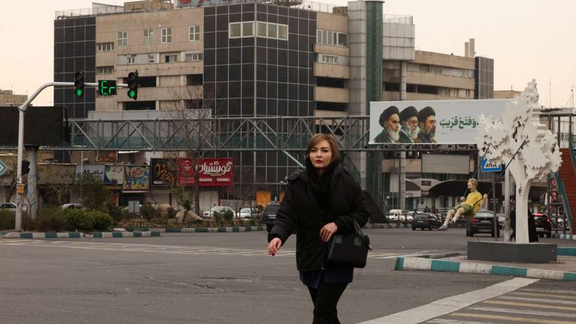 A woman walks across the street, with a banner of all three leaders of Iran, late Ruhollah Khomeini, late Ayatollah Ali Khamenei, and Mojtaba Khamenei in the background, in Tehran