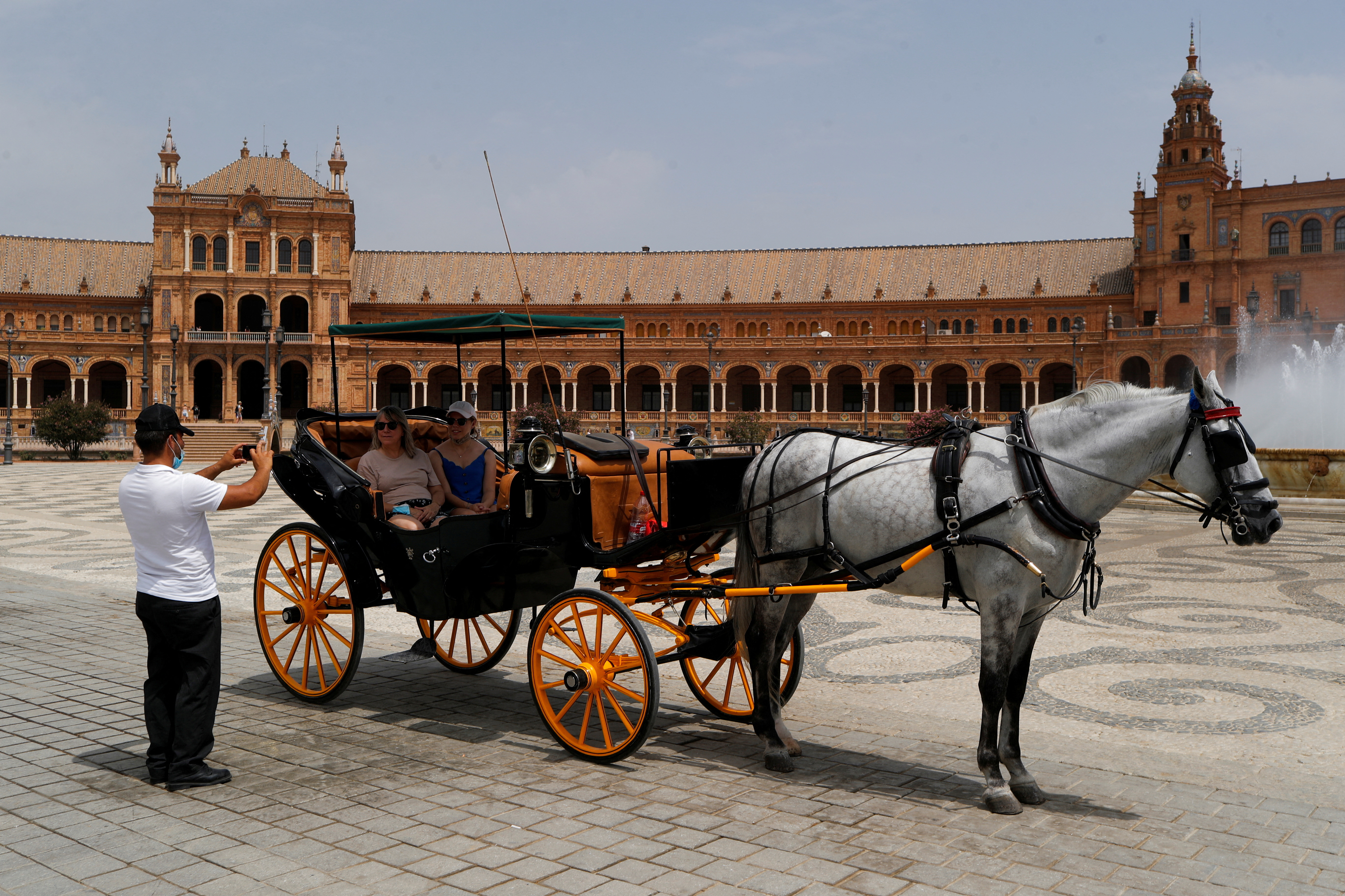 FILE PHOTO: A coachman takes a picture of tourists as they sit on a horse-drawn carriage at the Plaza de Espana, as a heatwave hits Spain, in Seville