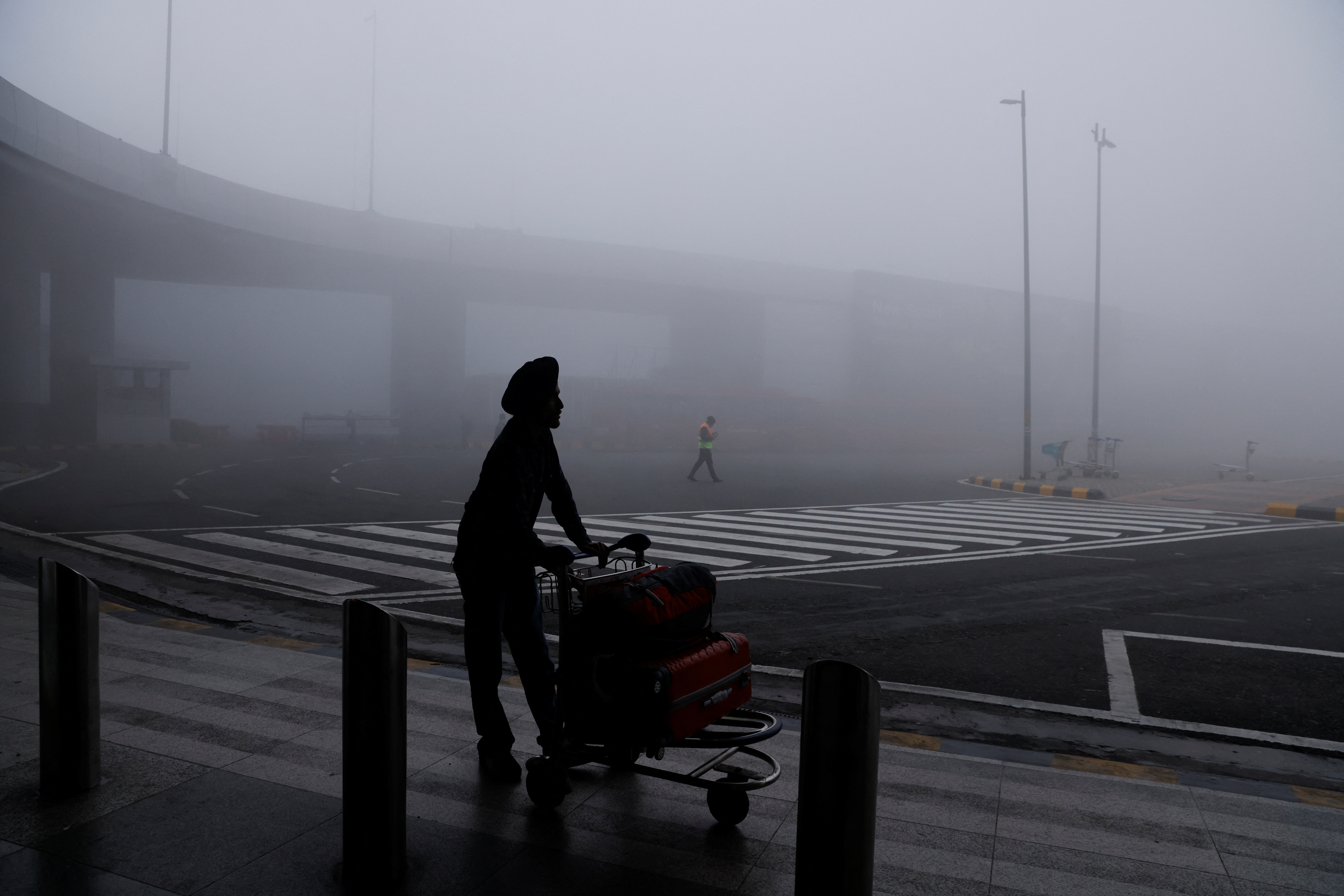 FILE PHOTO: A man is seen with his luggage cart amidst heavy fog at the Indira Gandhi International Airport in New Delhi