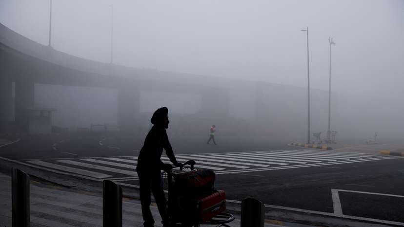 FILE PHOTO: A man is seen with his luggage cart amidst heavy fog at the Indira Gandhi International Airport in New Delhi