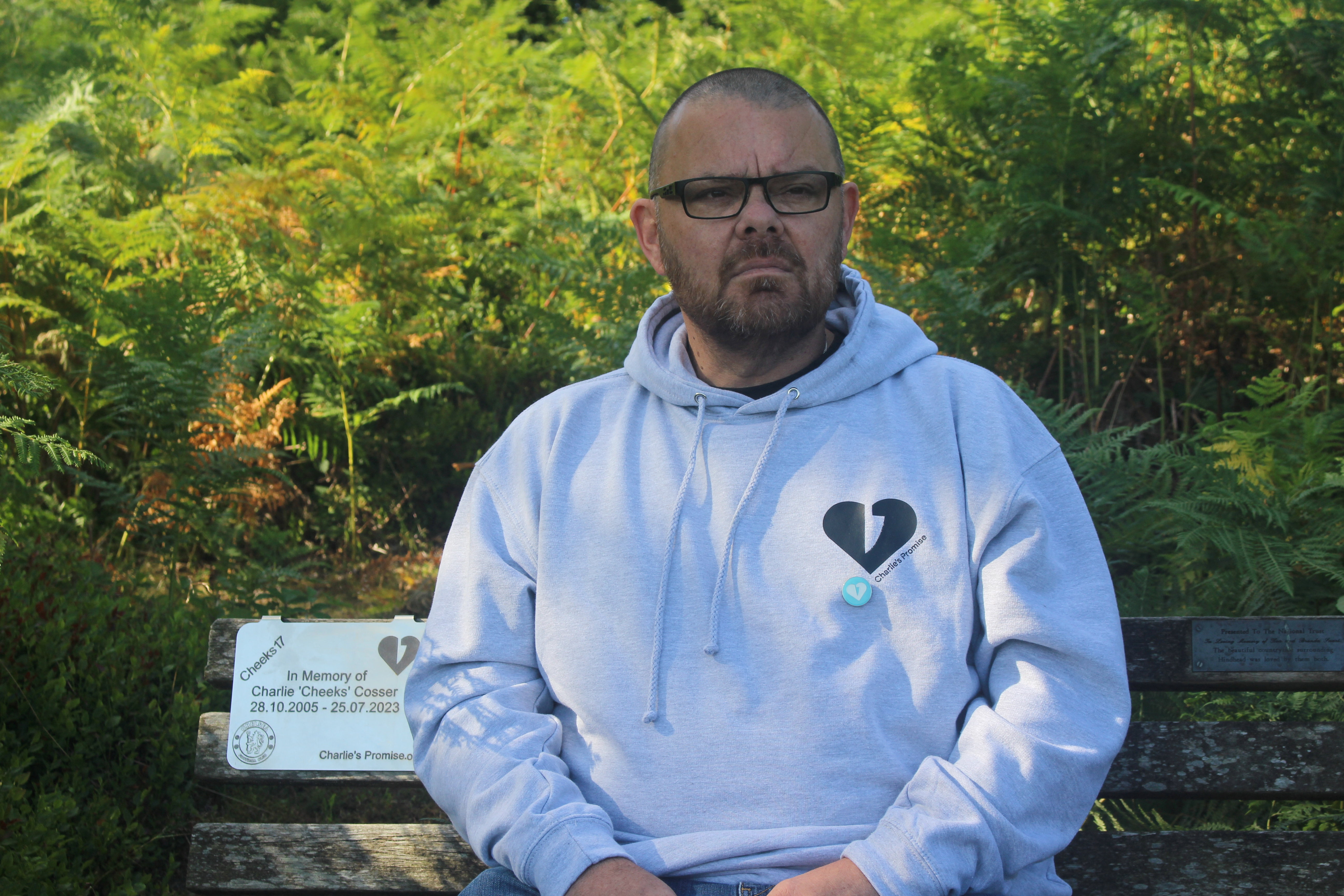 Martin Cosser sits on a memorial bench with a plaque honouring his son Charlie, at Devil's Punch Bowl, in Surrey