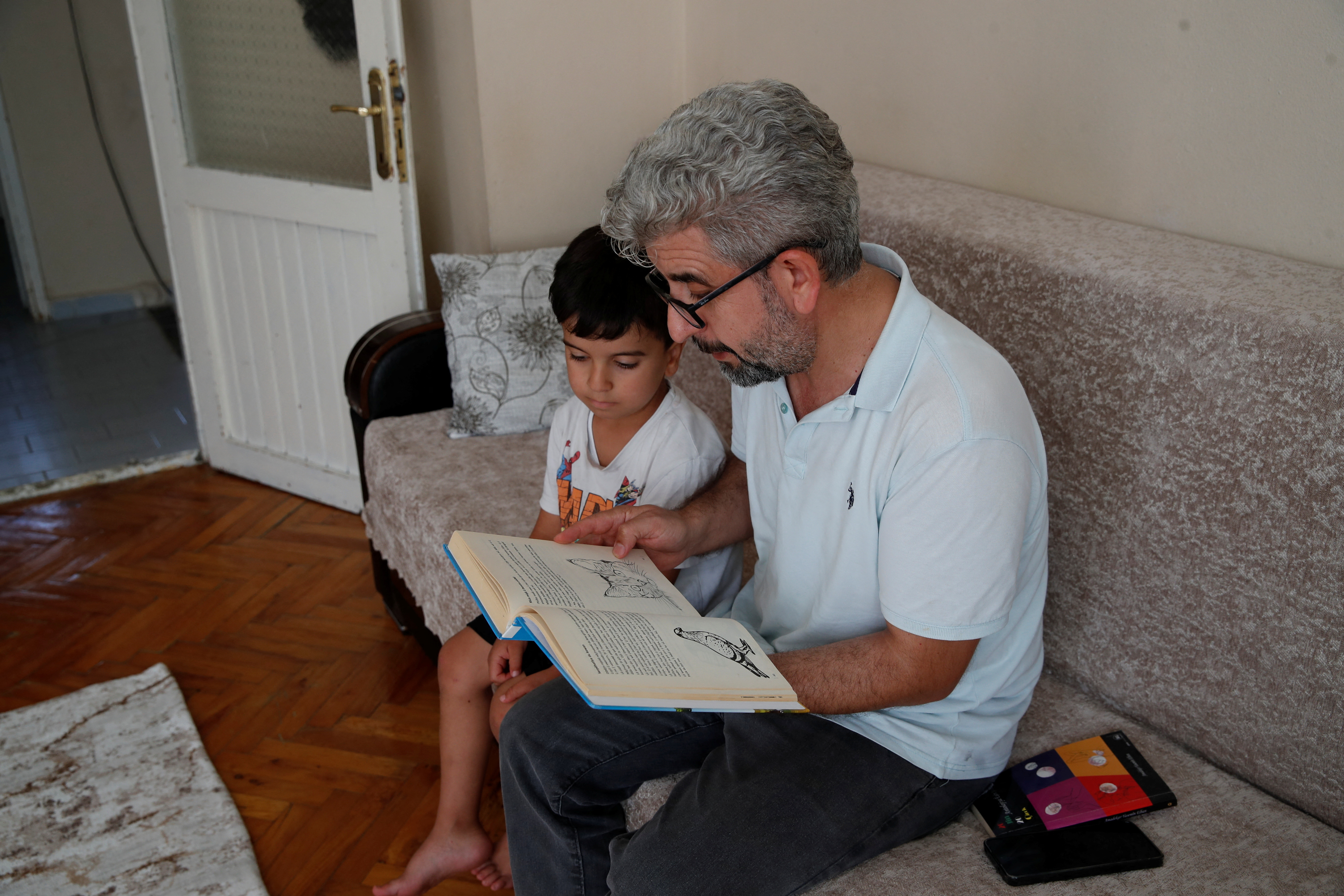 Nevzat Yesilbagdan reads a book in Kurdish to his son Muhammed Mesrur at their home in Istanbul