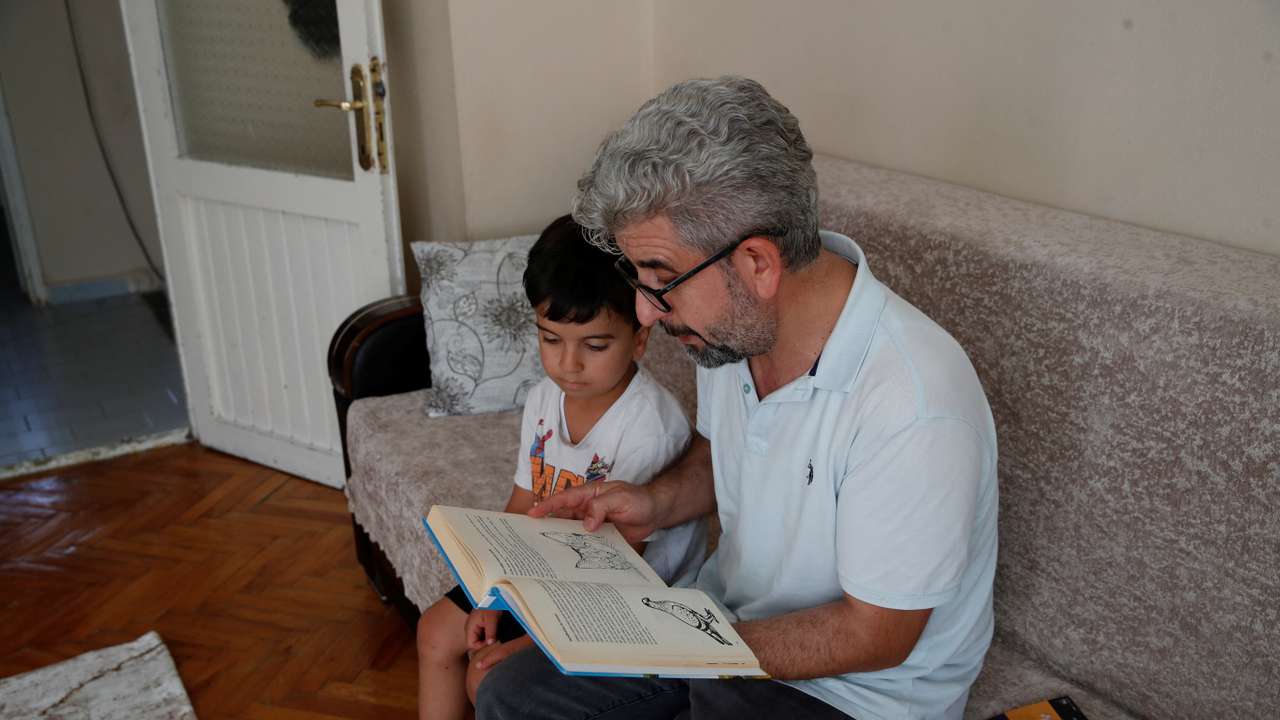 Nevzat Yesilbagdan reads a book in Kurdish to his son Muhammed Mesrur at their home in Istanbul