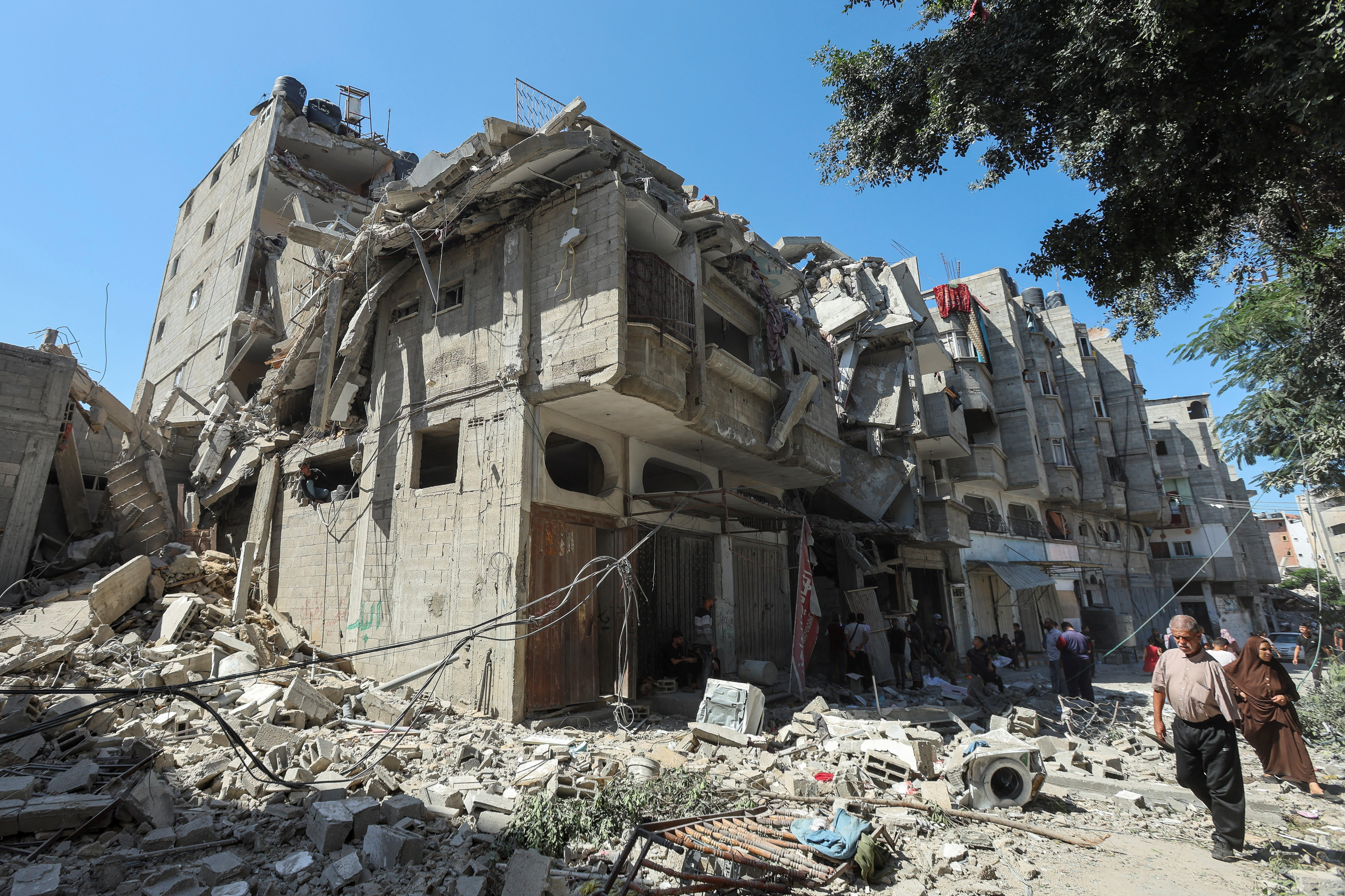 Palestinians walk past a house hit in an Israeli strike, amid the Israel-Hamas conflict, in Bureij refugee camp, in the central Gaza Strip