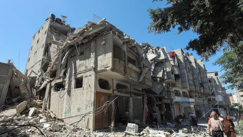 Palestinians walk past a house hit in an Israeli strike, amid the Israel-Hamas conflict, in Bureij refugee camp, in the central Gaza Strip