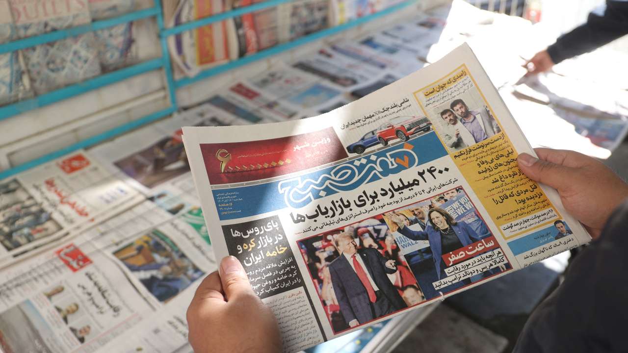 An Iranian man looks at a newspaper with a picture of Trump and Harris, in Tehran