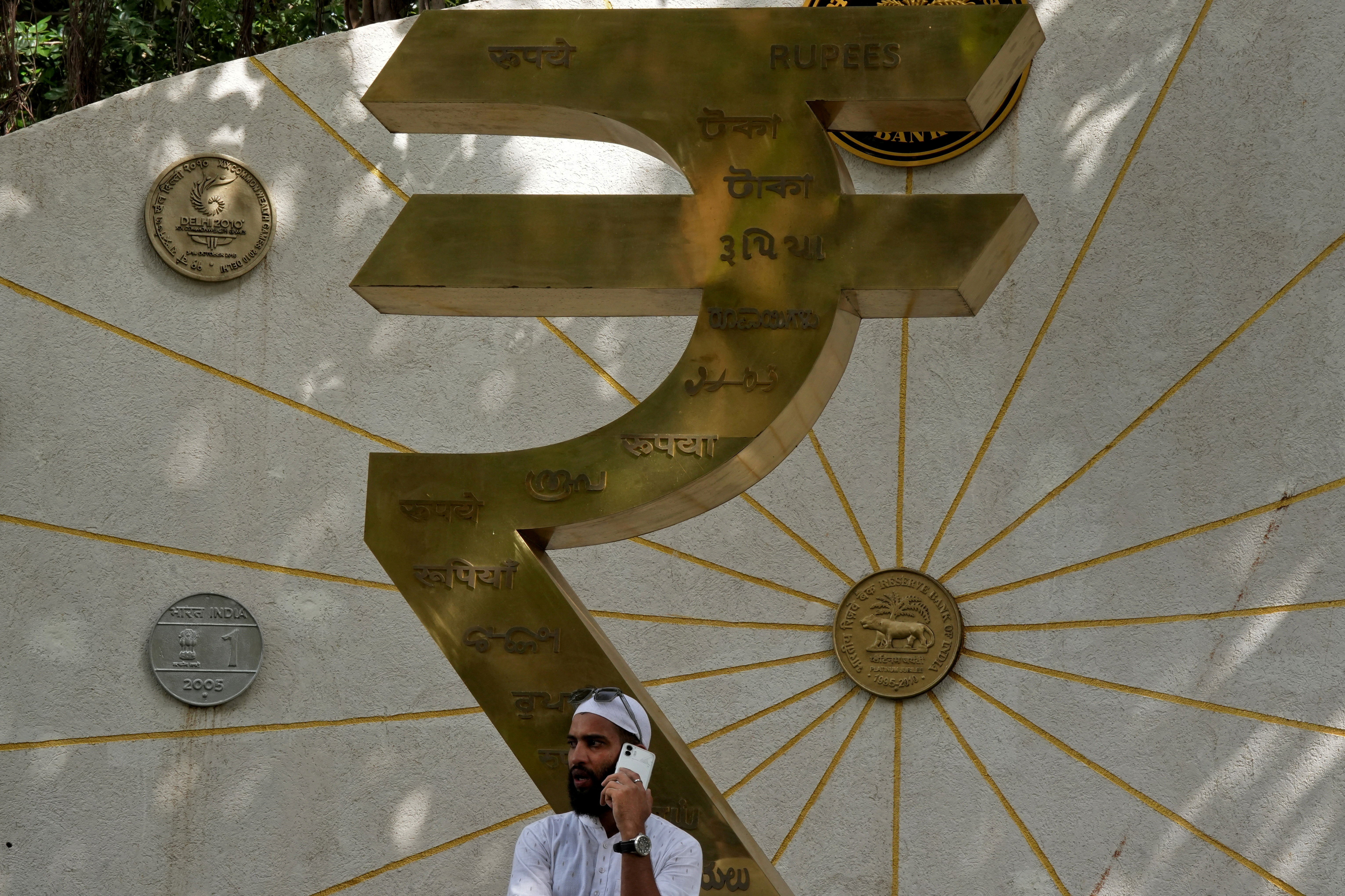 FILE PHOTO: A man speaks on his mobile phone next to an installation of the Rupee logo and Indian currency coins in Mumbai