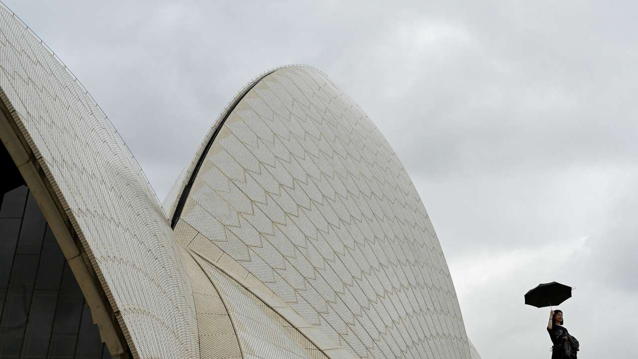 A woman holds up an umbrella at the Sydney Opera House during cloudy and rainy weather conditions in Sydney