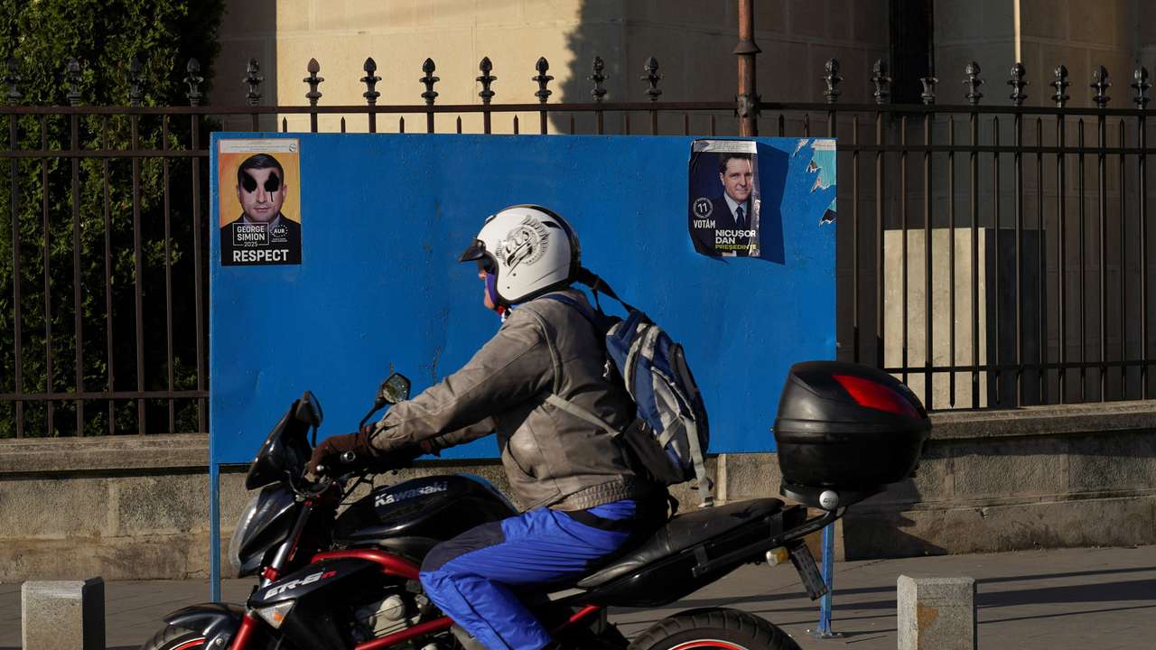 A motorcycle passes by electoral posters of Nicusor Dan and George Simion in Bucharest