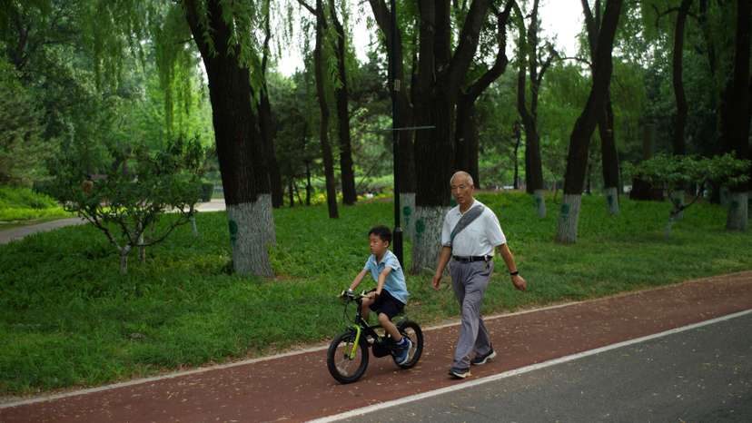 An elderly person walks next to a child at a park on a summer day in Beijing