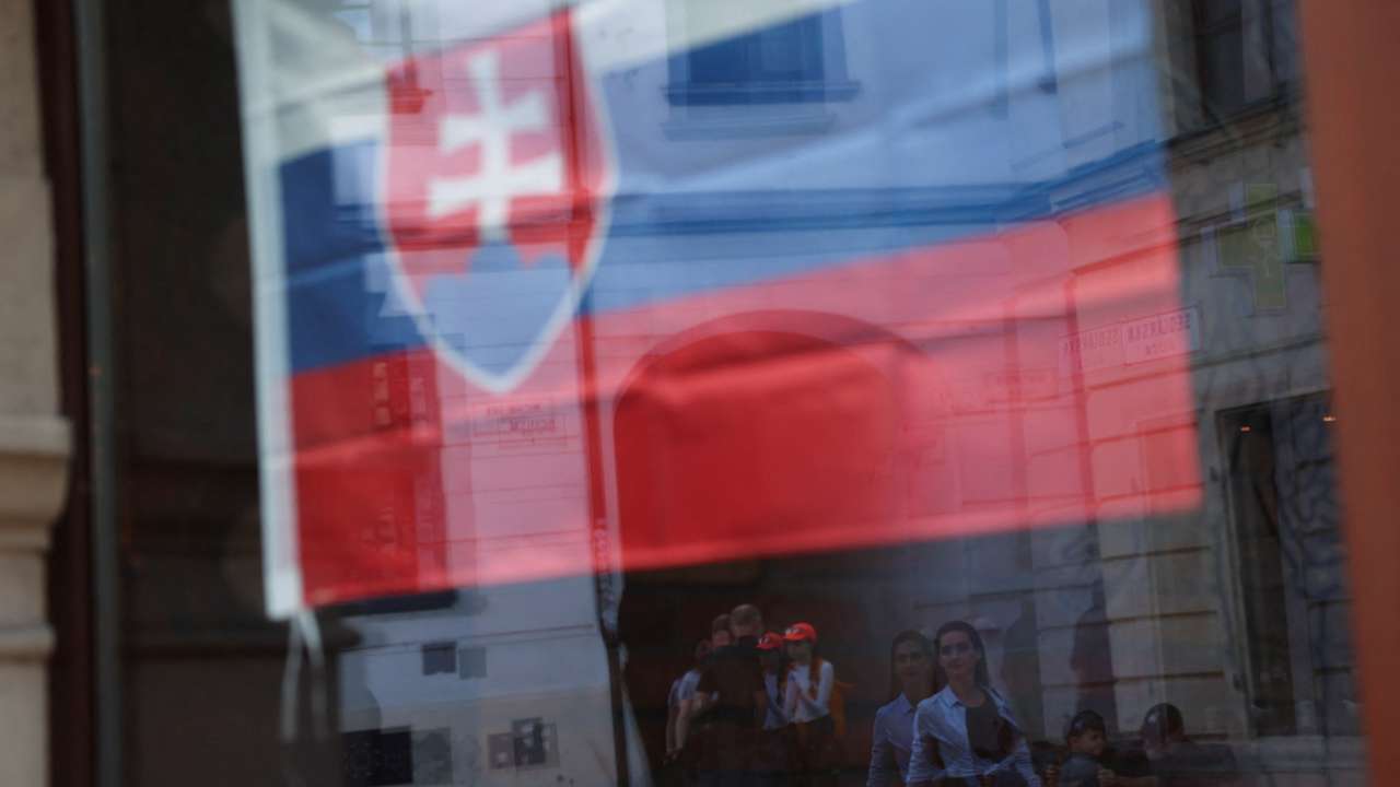 People are reflected in a window adorned with a Slovakian flag