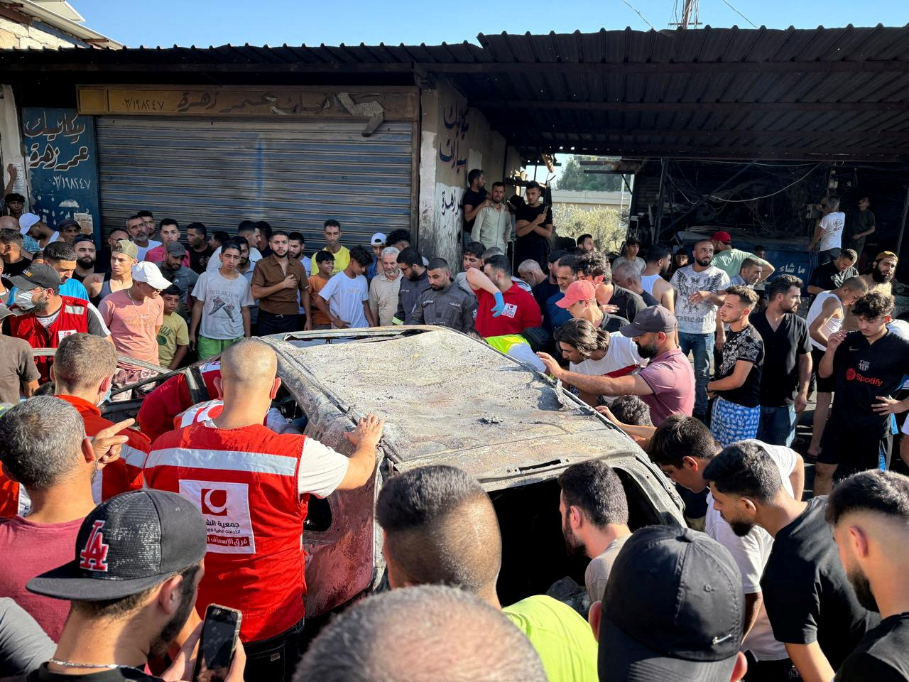 People gather near a damaged car after the Israeli military said in a statement it struck a "key" figure from Palestinian militant group Hamas, in Ayrounieh