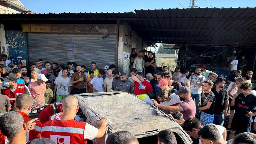 People gather near a damaged car after the Israeli military said in a statement it struck a "key" figure from Palestinian militant group Hamas, in Ayrounieh