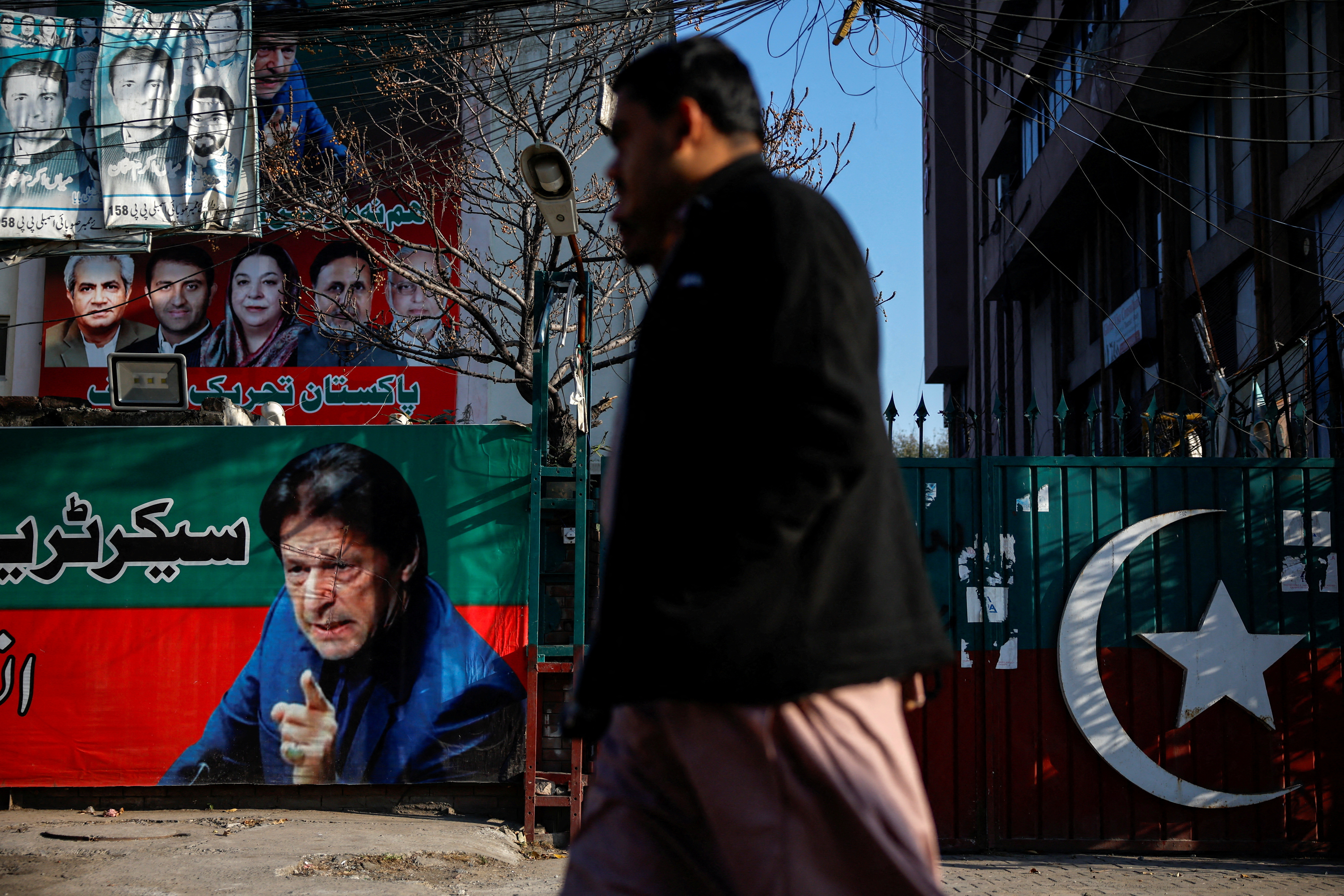 FILE PHOTO: People walk past a banner with a picture of the former Prime Minister Imran Khan outside the party office of Pakistan Tehreek-e-Insaf (PTI), a day after the general election, in Lahore