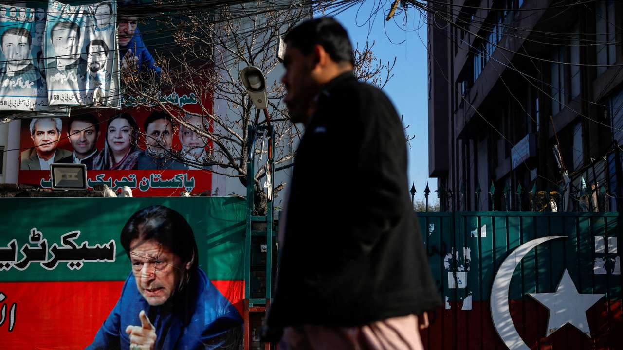 FILE PHOTO: People walk past a banner with a picture of the former Prime Minister Imran Khan outside the party office of Pakistan Tehreek-e-Insaf (PTI), a day after the general election, in Lahore