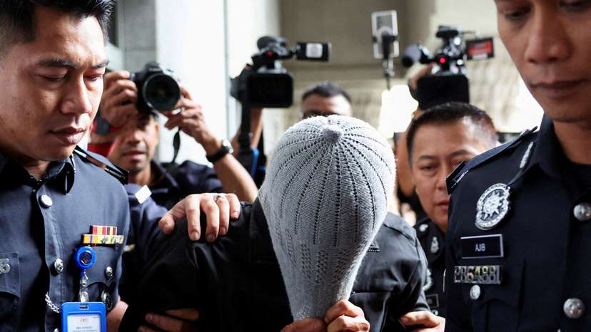 A man linked to Global Ikhwan Service and Business Holdings (GISB) covers his face as he is escorted by police officers after being charged in a court in Putrajaya