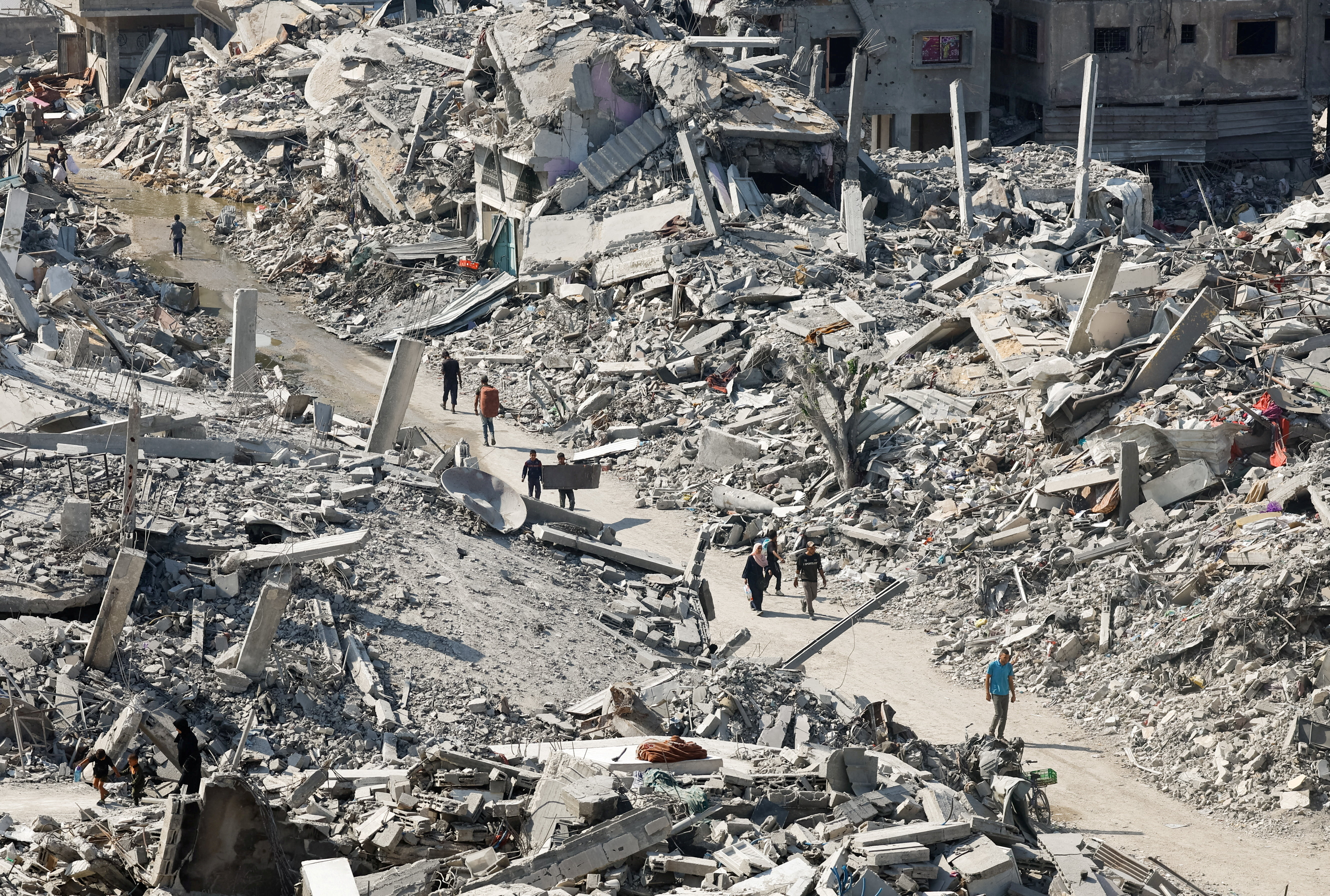 Palestinians walk past the rubble of destroyed buildings, amid a ceasefire between Israel and Hamas, in Gaza City