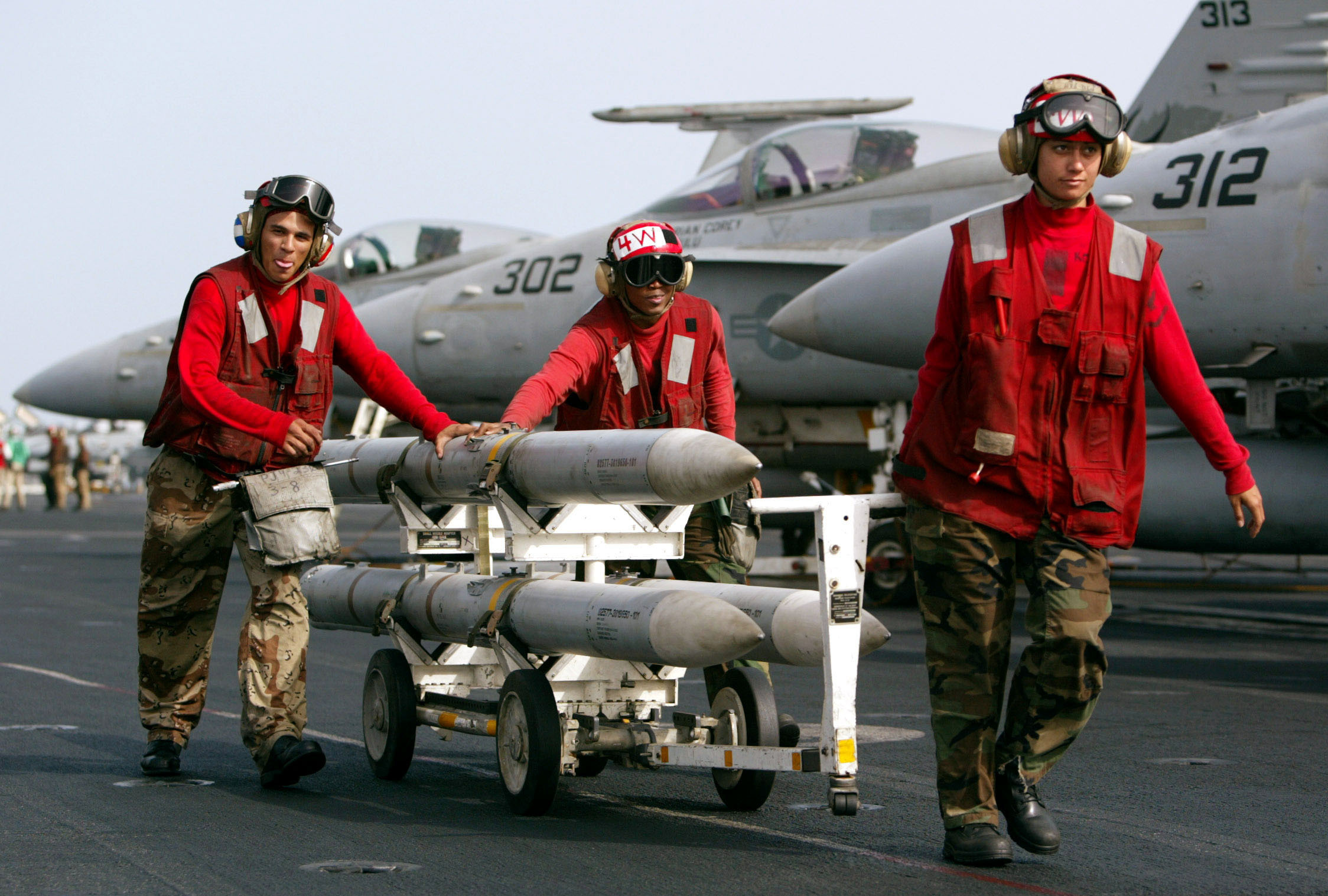 AIM-120 AMRAAM air-to-air intercept missiles are wheeled past fighter jets on the deck of the USS Ki..