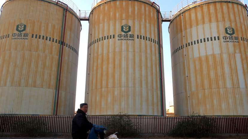 FILE PHOTO: Man cycles past storage facilities of China's state grain stockpiler Sinograin near Tianjin port