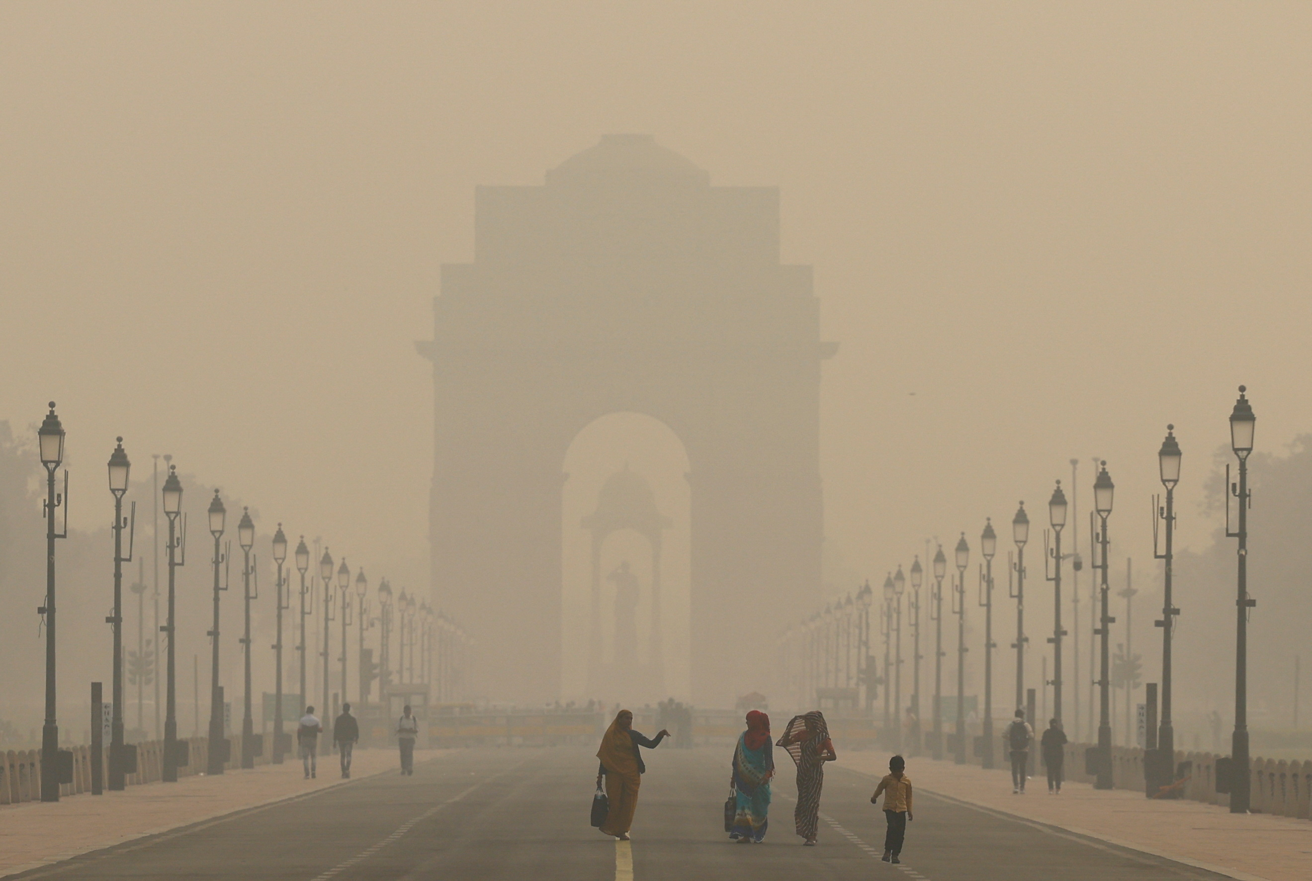 Women walk on a road near India Gate as the sky is enveloped with smog after Delhi's air quality worsened due to air pollution, in New Delhi